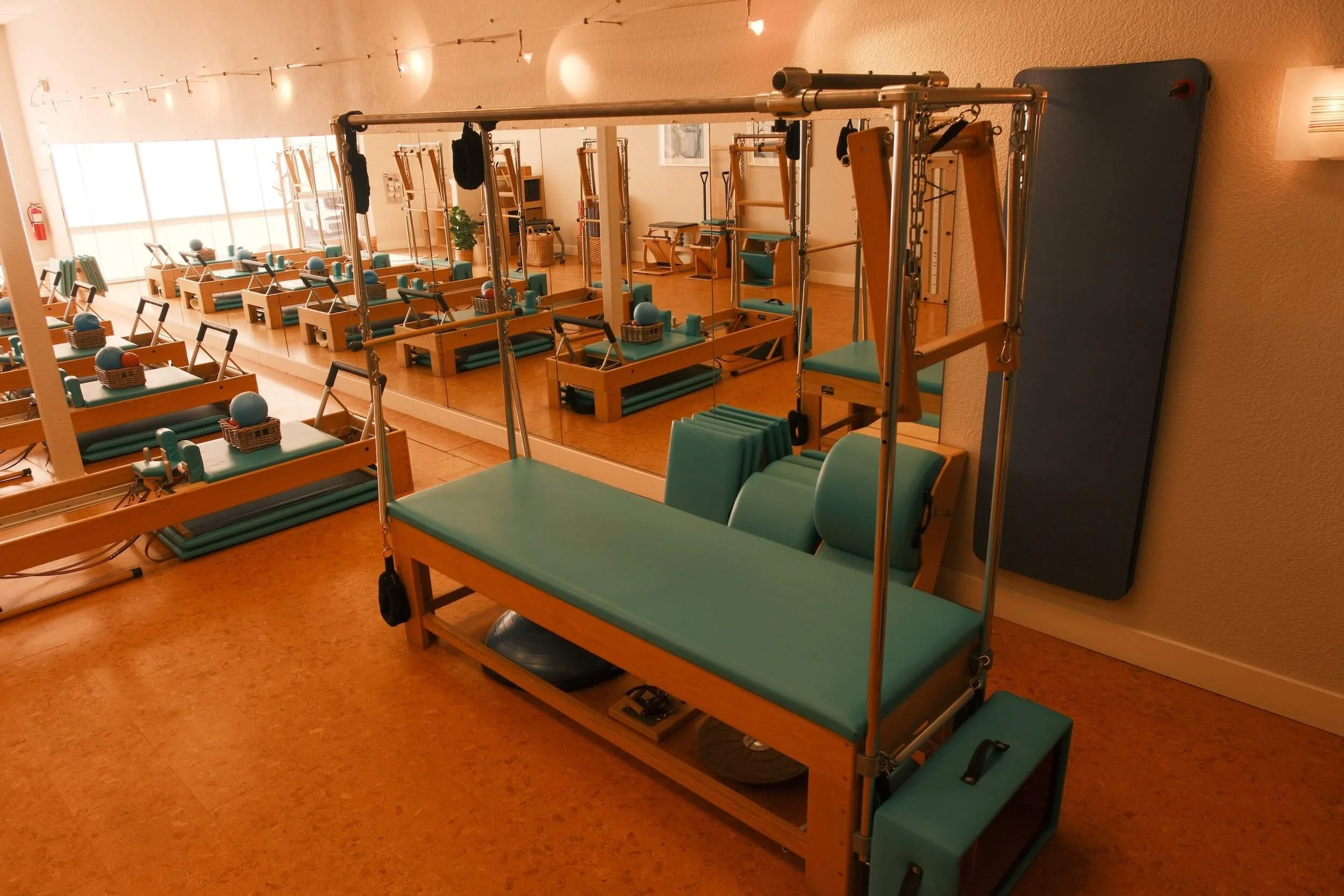 Rehabilitation therapy room with wooden equipment, mats, and chairs, reflected in a large mirror on the wall.