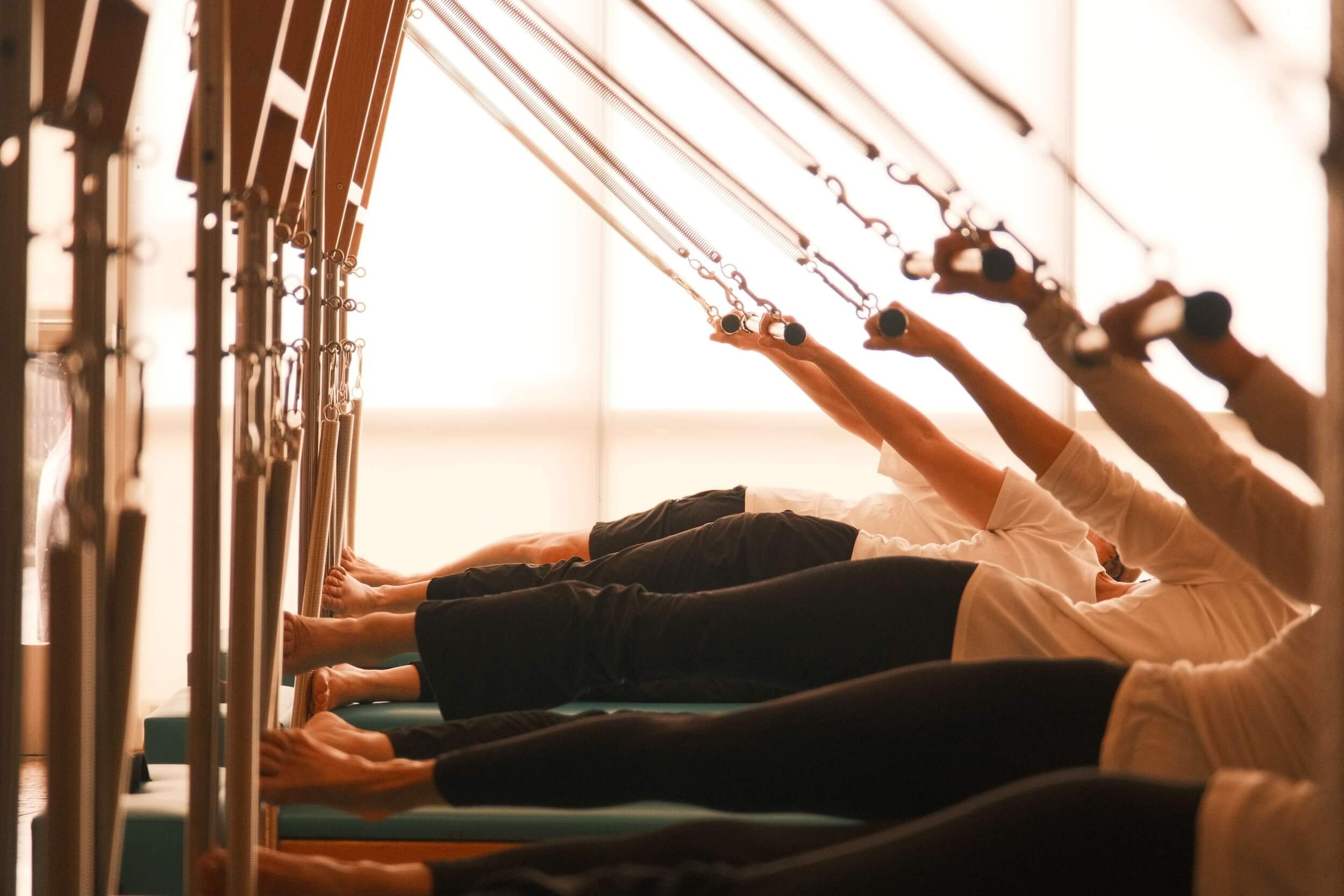 People practicing yoga in a studio, lying on mats and stretching with their arms extended upward.