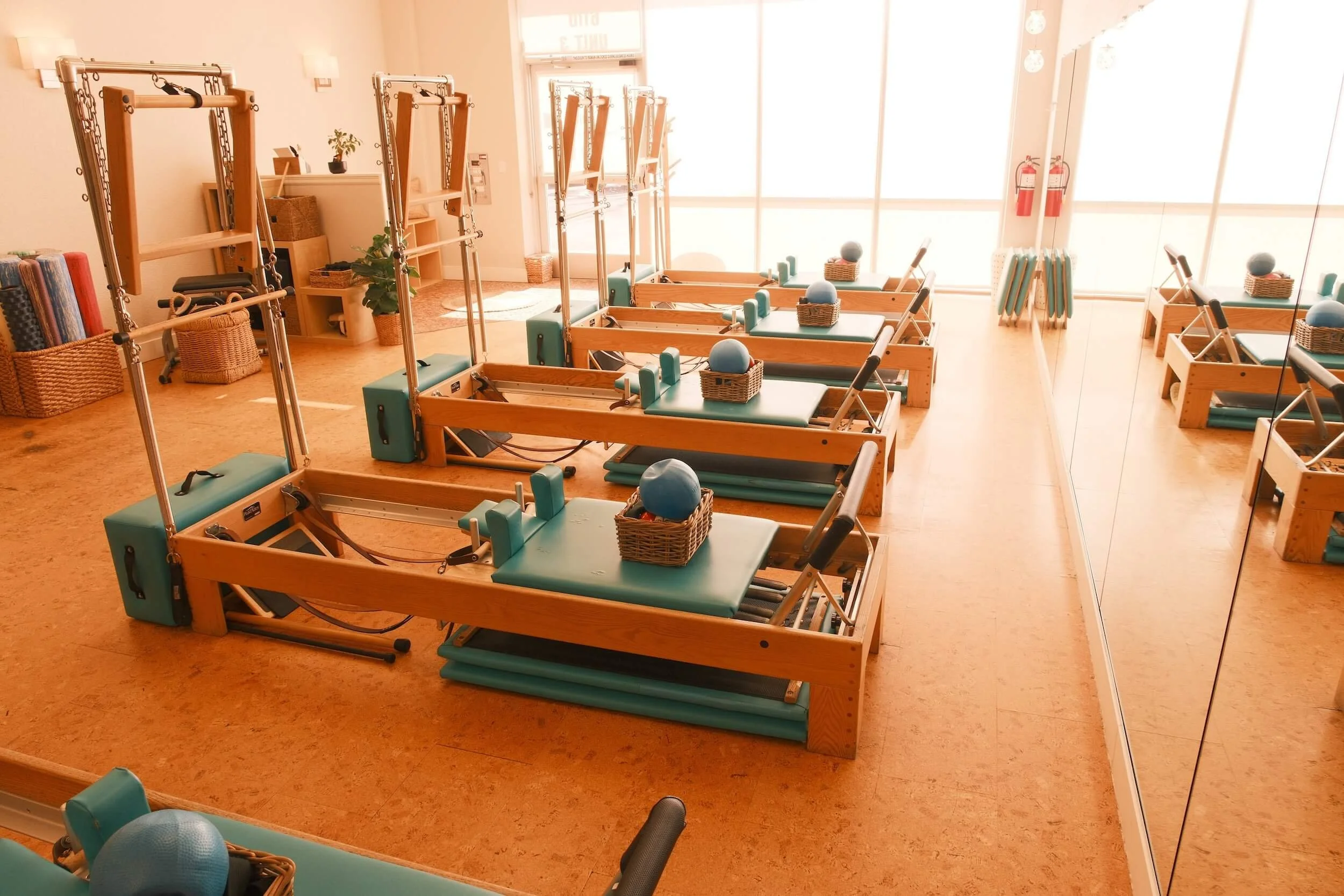 Pilates reformer machines with blue pads and balls in a well-lit fitness studio.