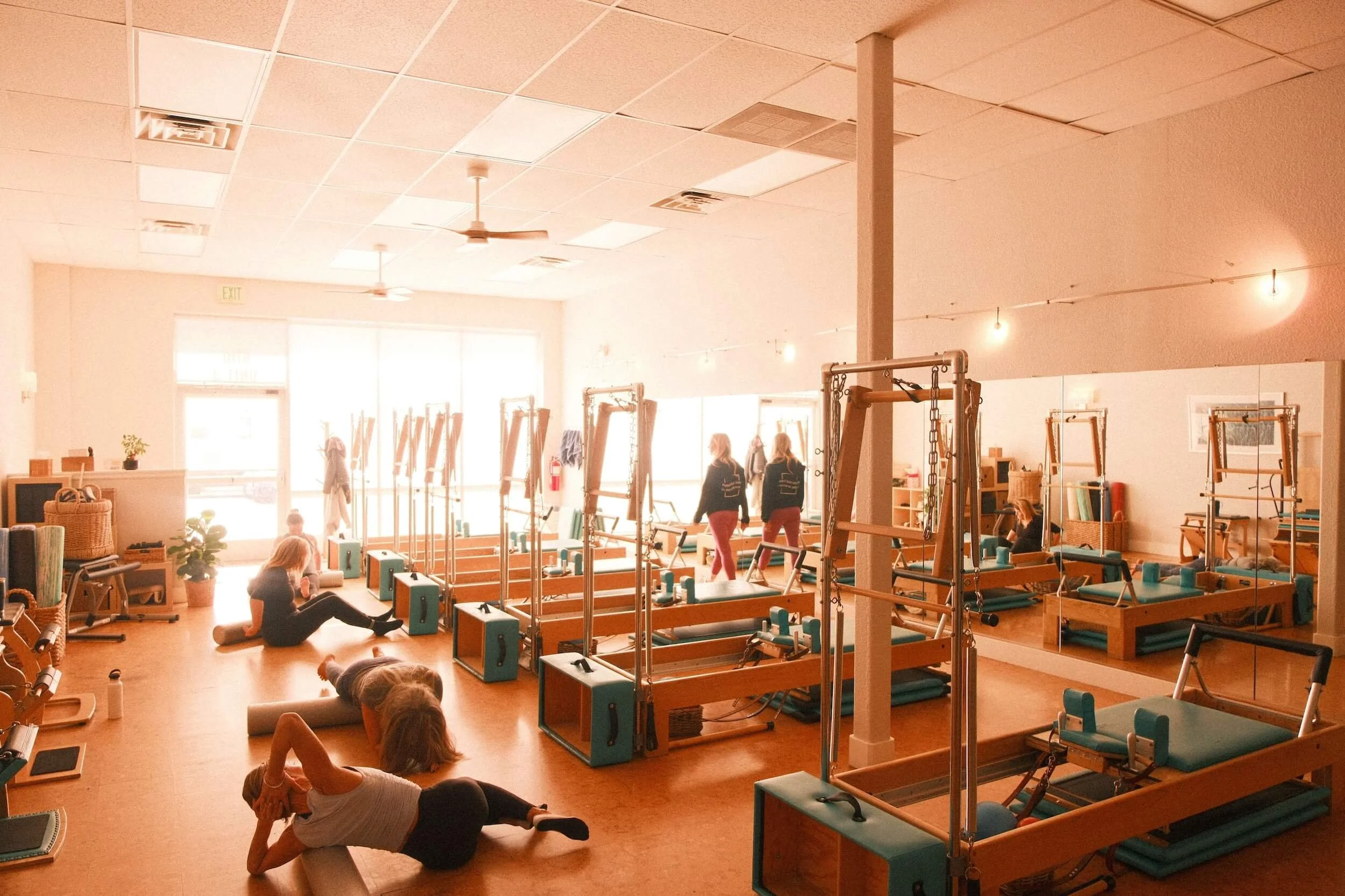 Pilates class in studio with women using reformer machines and practicing stretches on the floor.