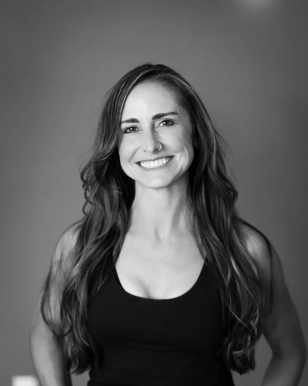 Black and white portrait of a smiling woman with long wavy hair wearing a black sleeveless top.