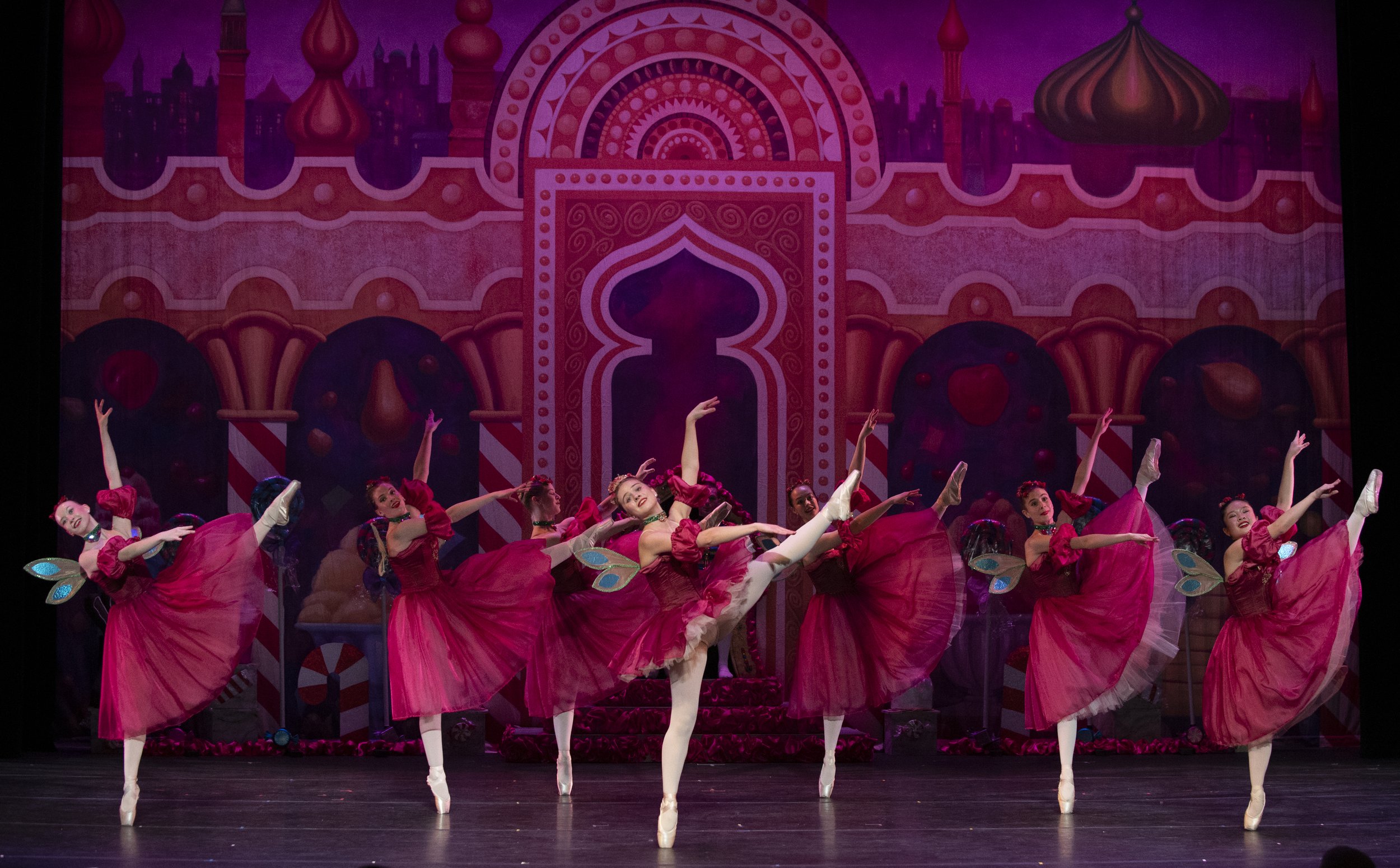 Ballet dancers in pink tutus performing on stage with a colorful, ornate backdrop resembling a Middle Eastern palace.