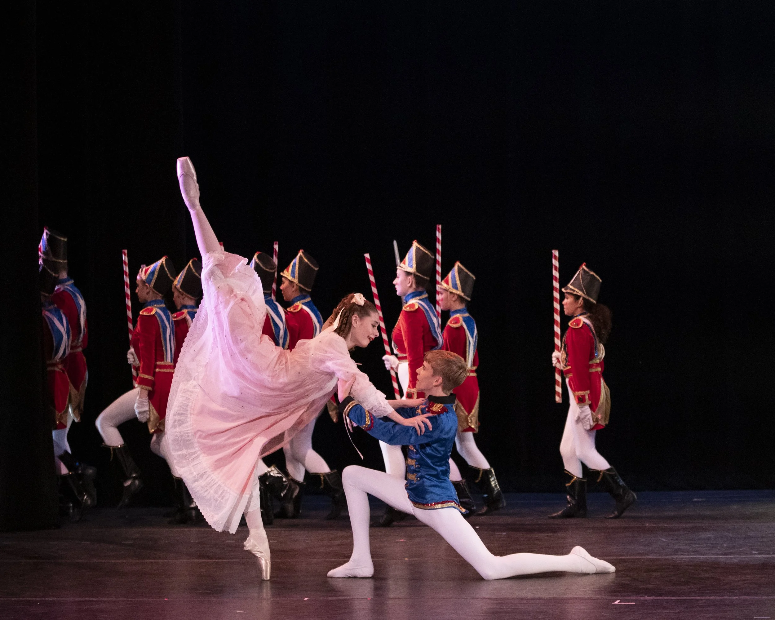 Ballet dancers performing on stage with soldiers in colorful costumes in the background.