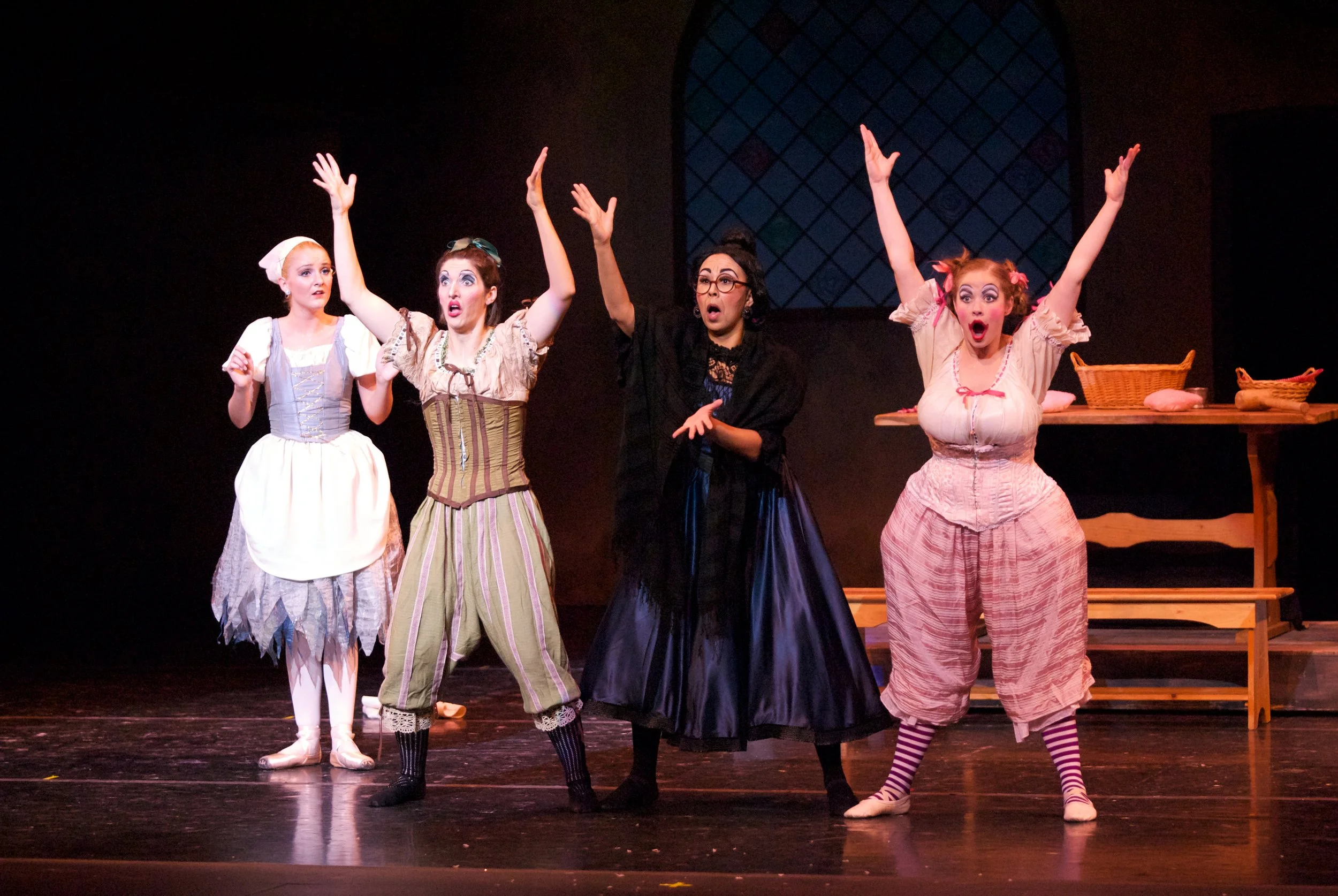 Four women in theatrical costumes performing on stage with surprised and expressive reactions.