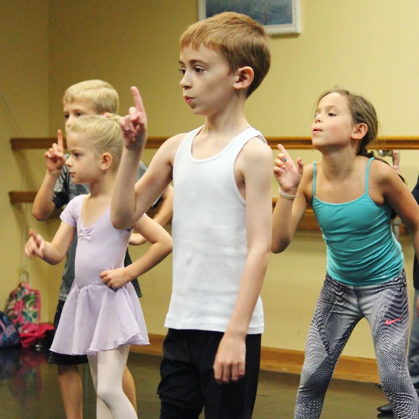 Children practicing ballet in a dance studio, some with hands raised in ballet positions.