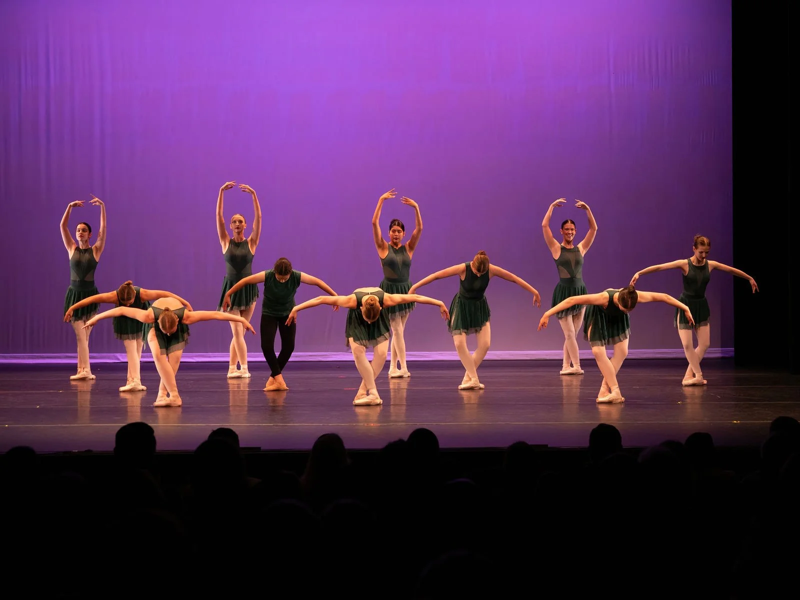 Group of ballet dancers performing on stage with a purple backdrop.