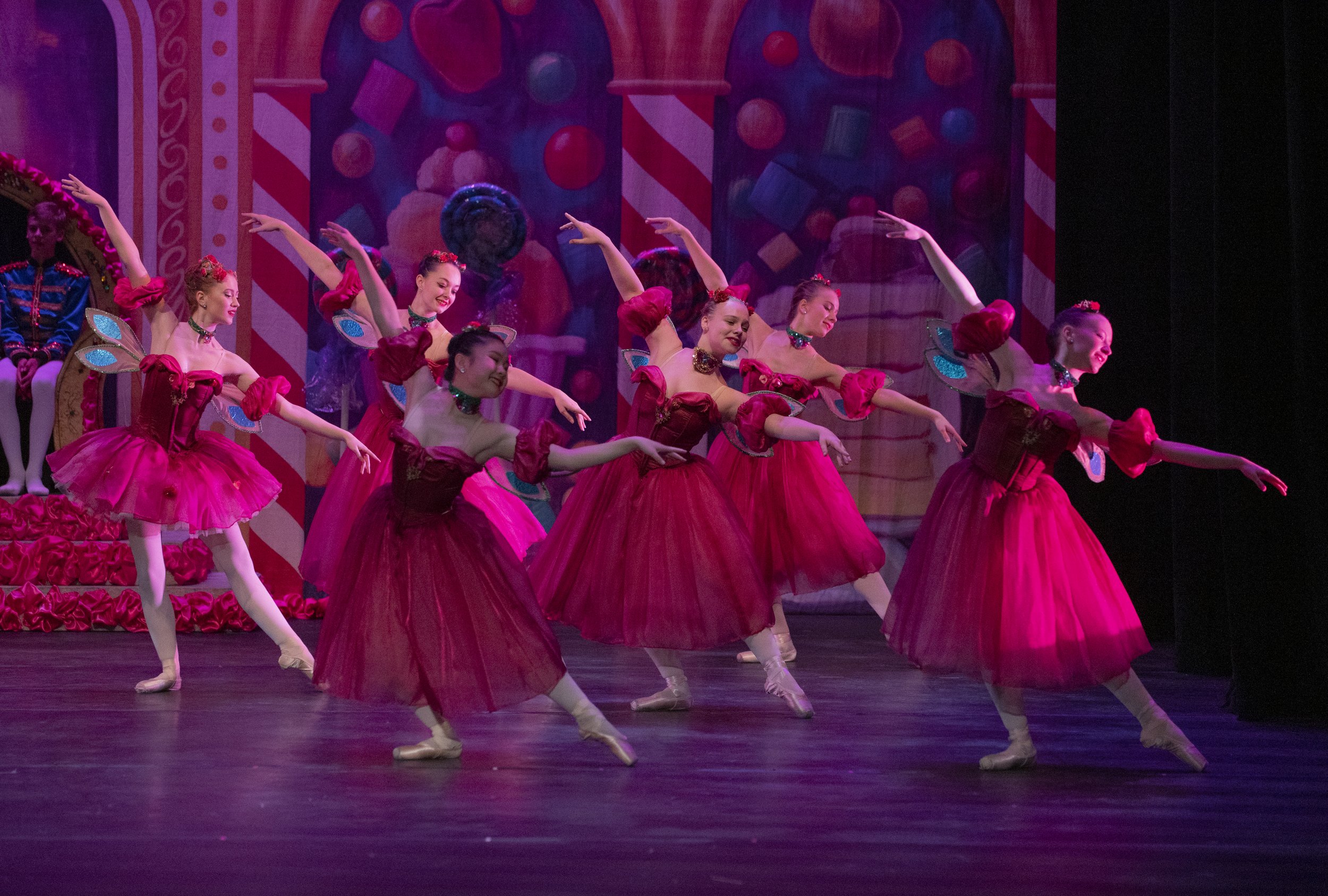 Ballet dancers in pink costumes performing on stage with a colorful candy-themed backdrop.
