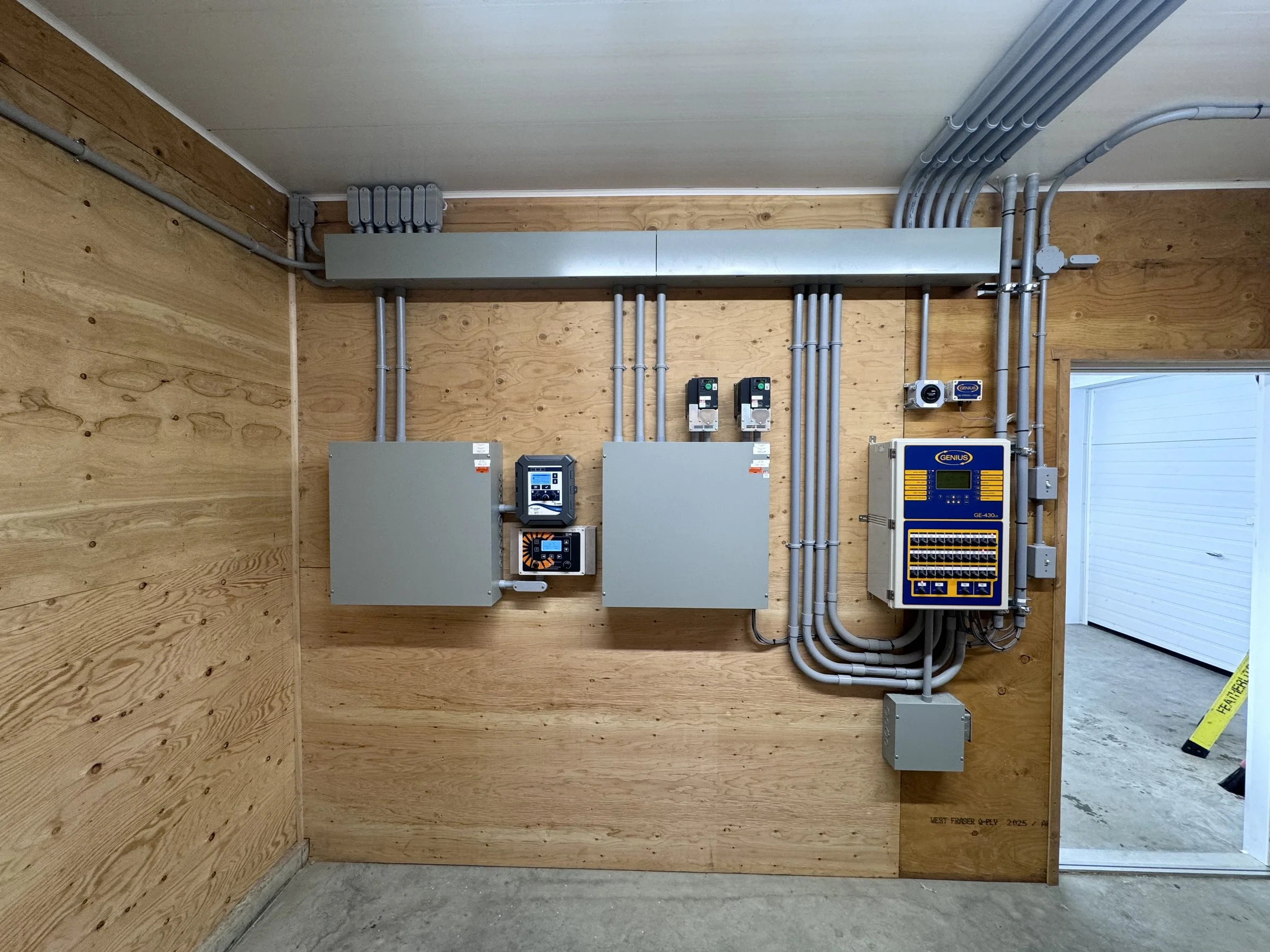 Electrical control panel and wiring mounted on a wooden wall in a utility room.