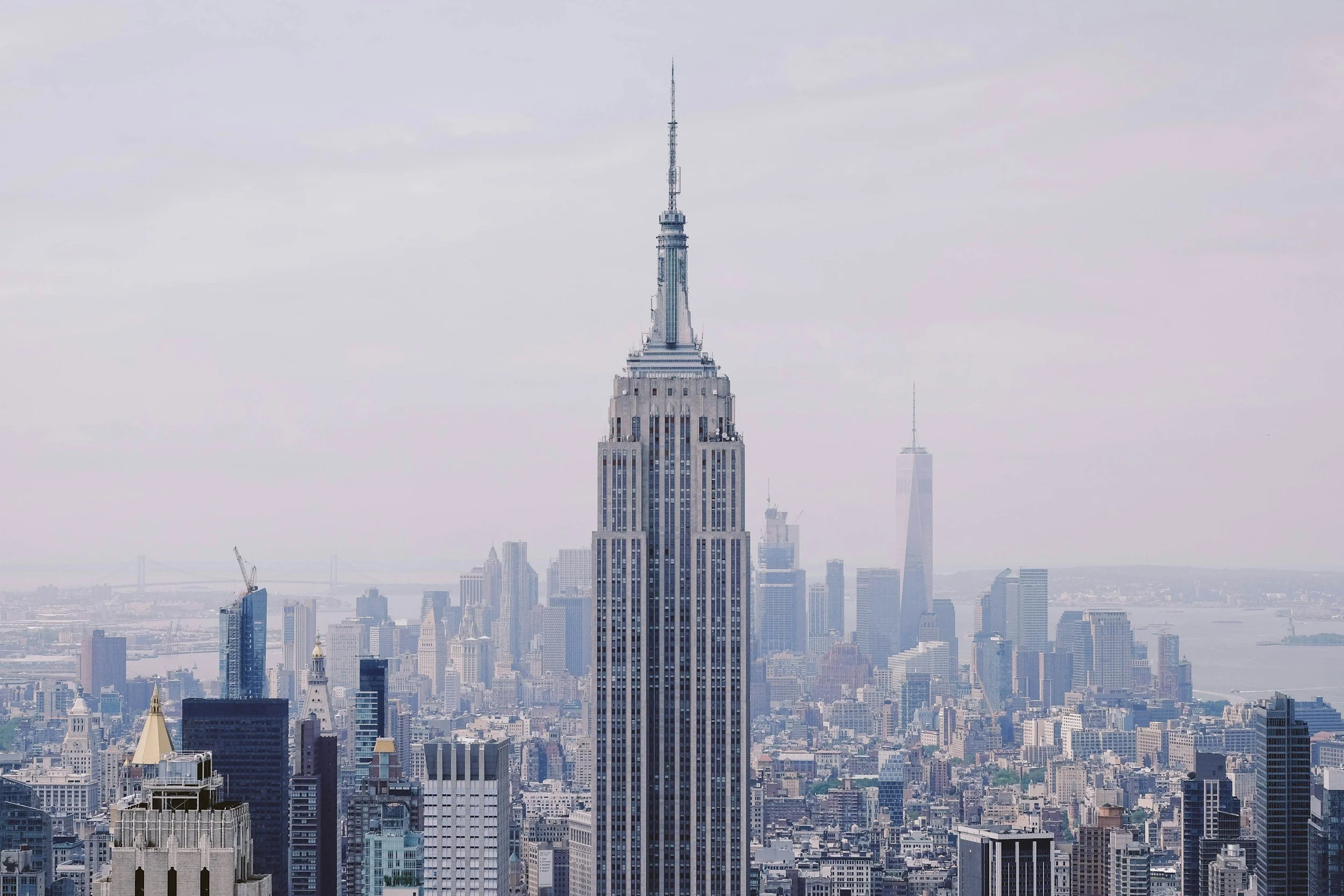 City skyline featuring the Empire State Building in New York City, with other skyscrapers and the Hudson River in the background.