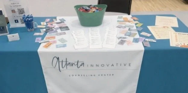 A table with a blue tablecloth, displaying various pamphlets and informational materials, with a banner reading 'Atlanta Innovative Counseling Center'.