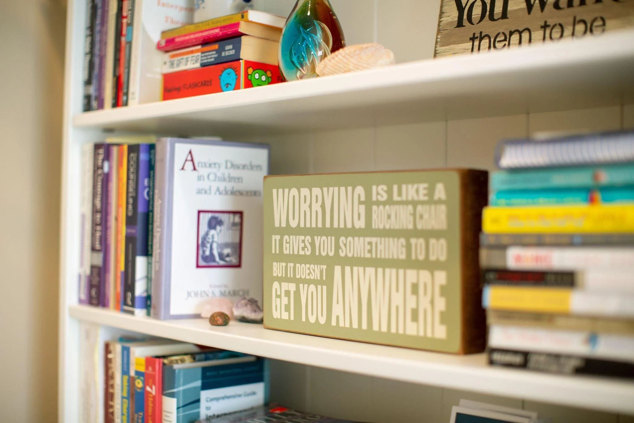 Bookshelf with numerous books, a decorative glass object, and a sign with text, in a room with beige walls.