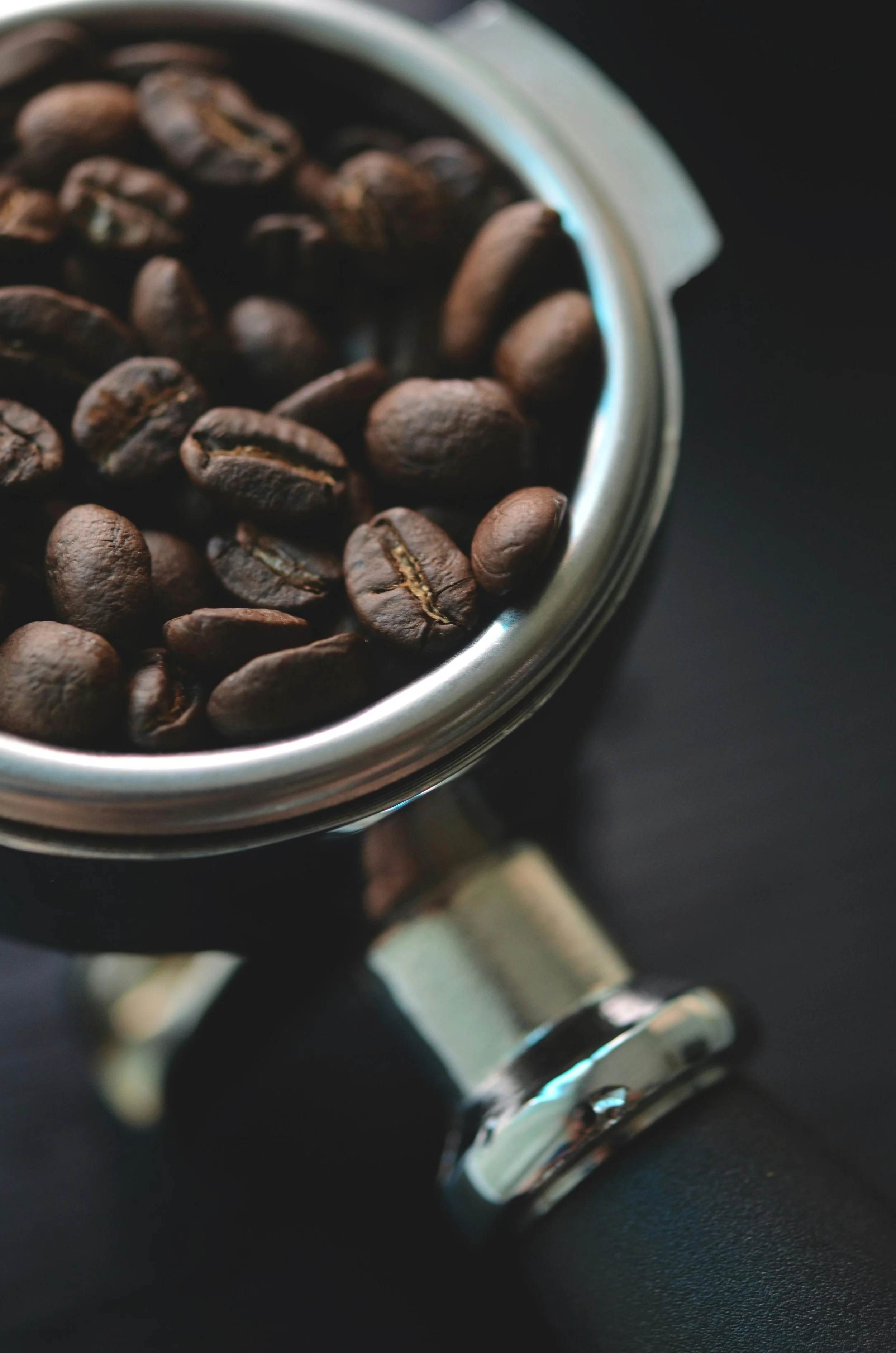 Close-up of a modern manual coffee grinder filled with roasted coffee beans on a black surface.