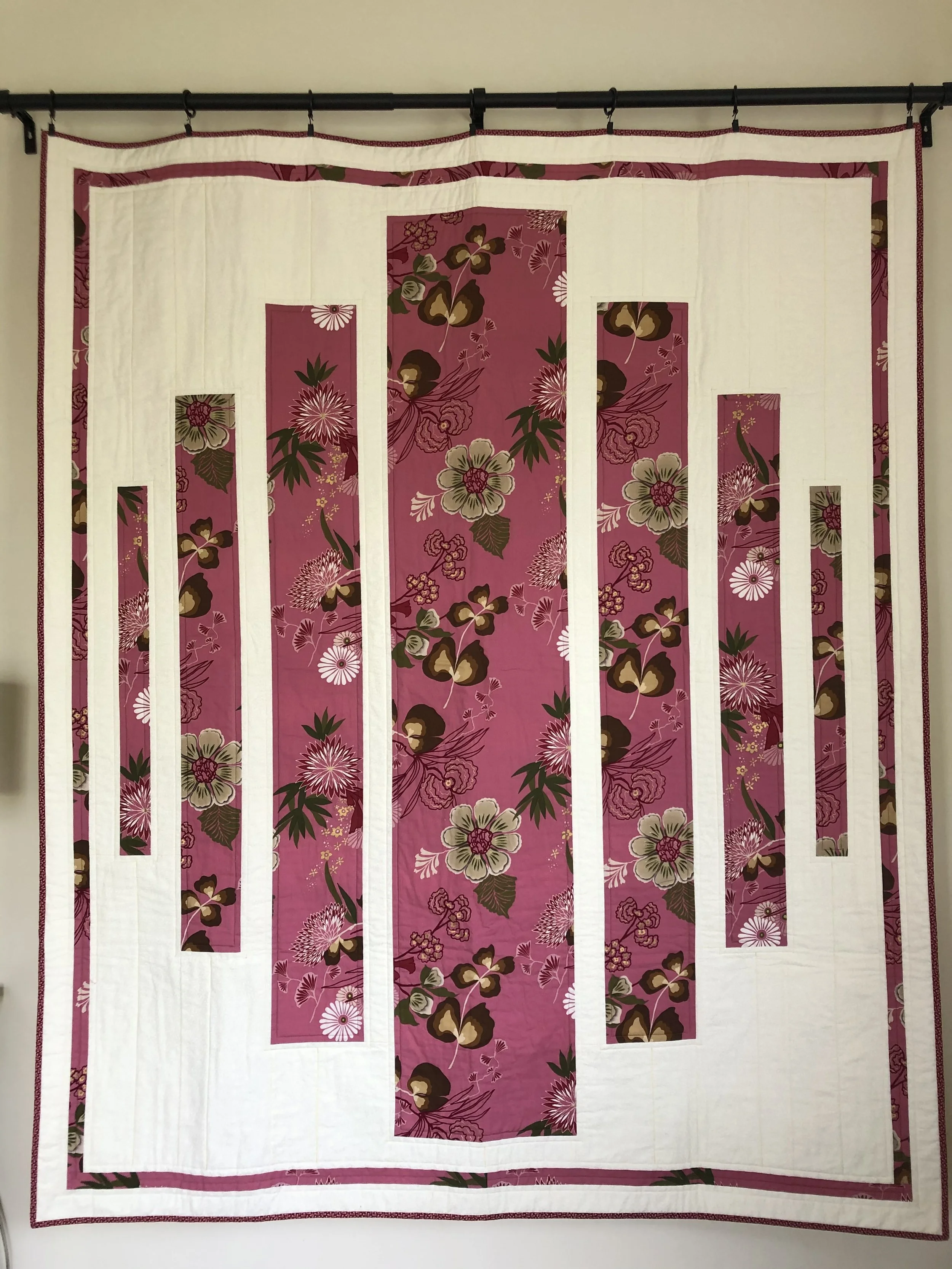 A quilt with a white background and vertical pink floral patterned strips arranged in a modern geometric design.