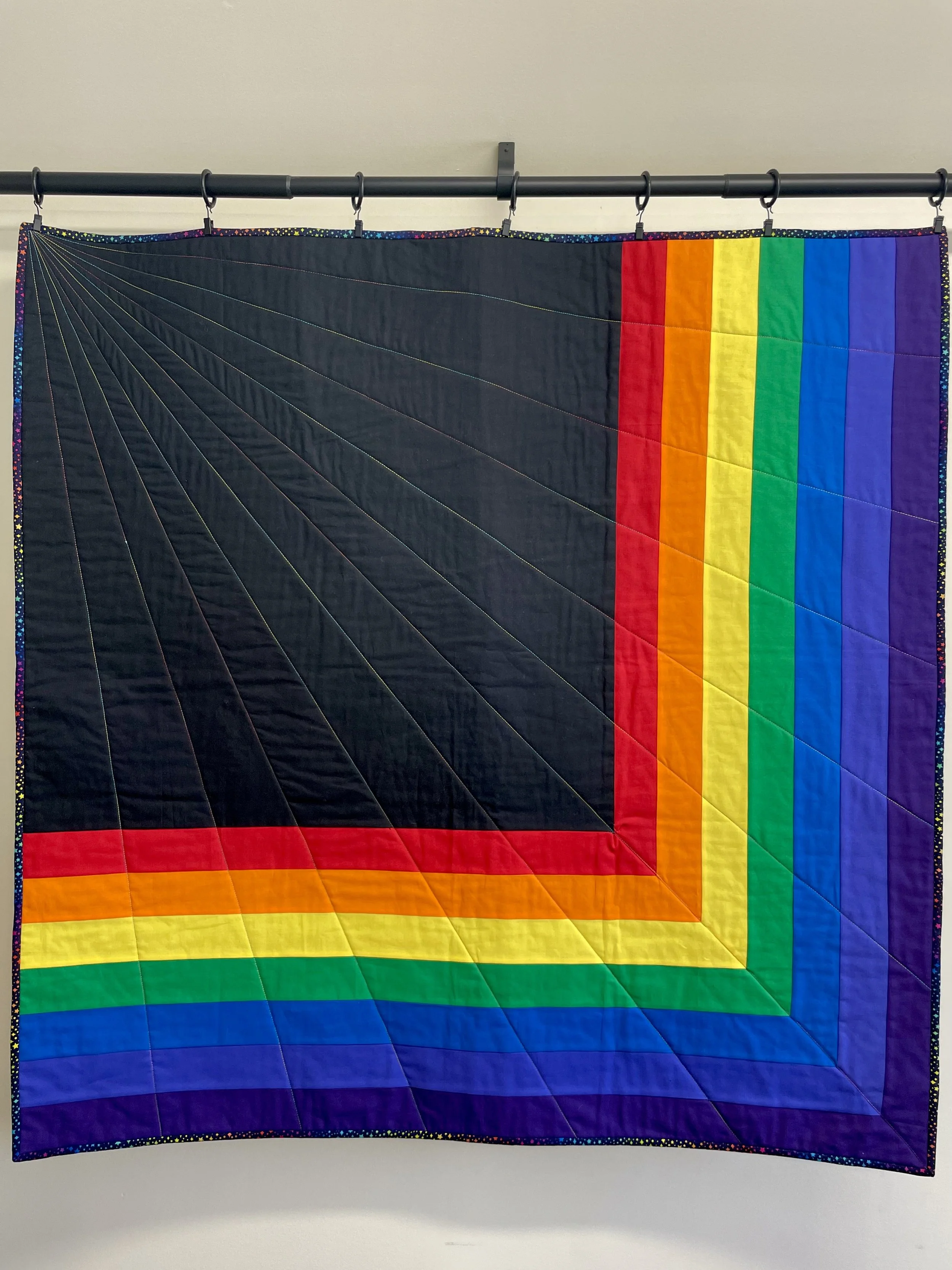 A quilt with a rainbow border and black center, featuring radiating lines and colorful stripes along the edges.