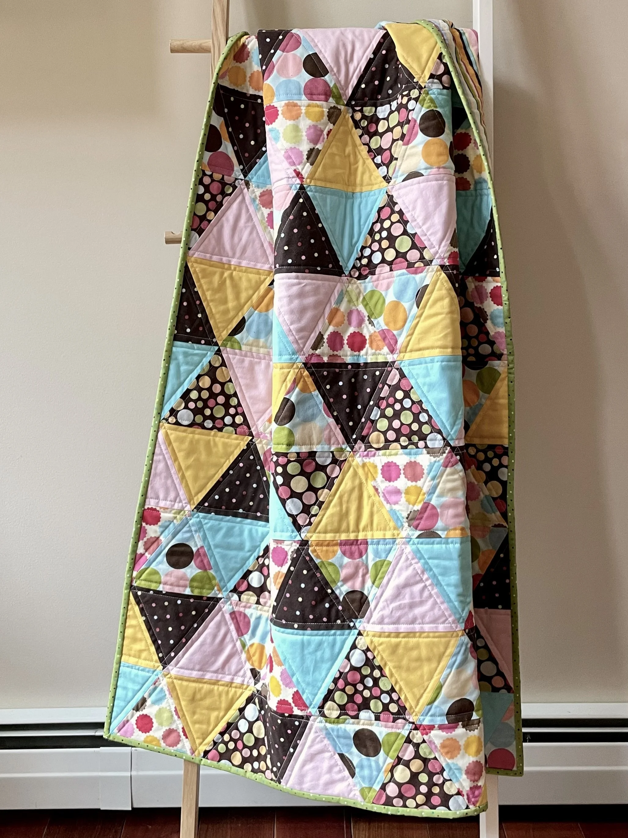 Colorful quilt with a pattern of triangles hanging on a wooden ladder.