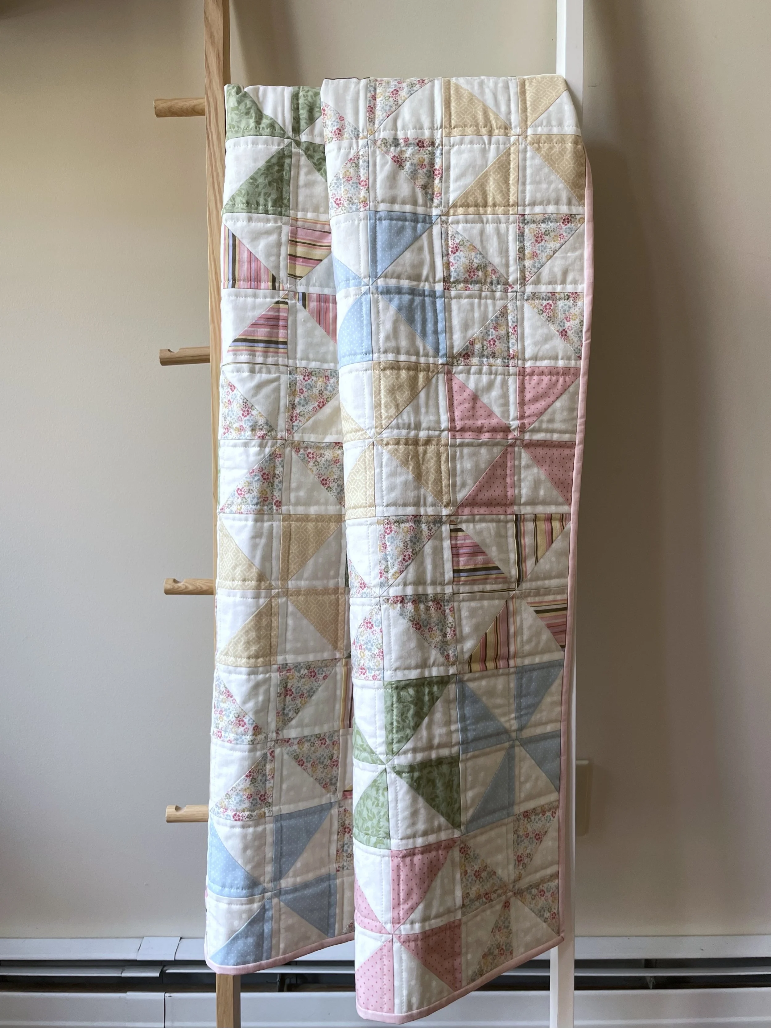 Colorful pinwheel quilt with various pastel-colored fabric squares hanging on a ladder.