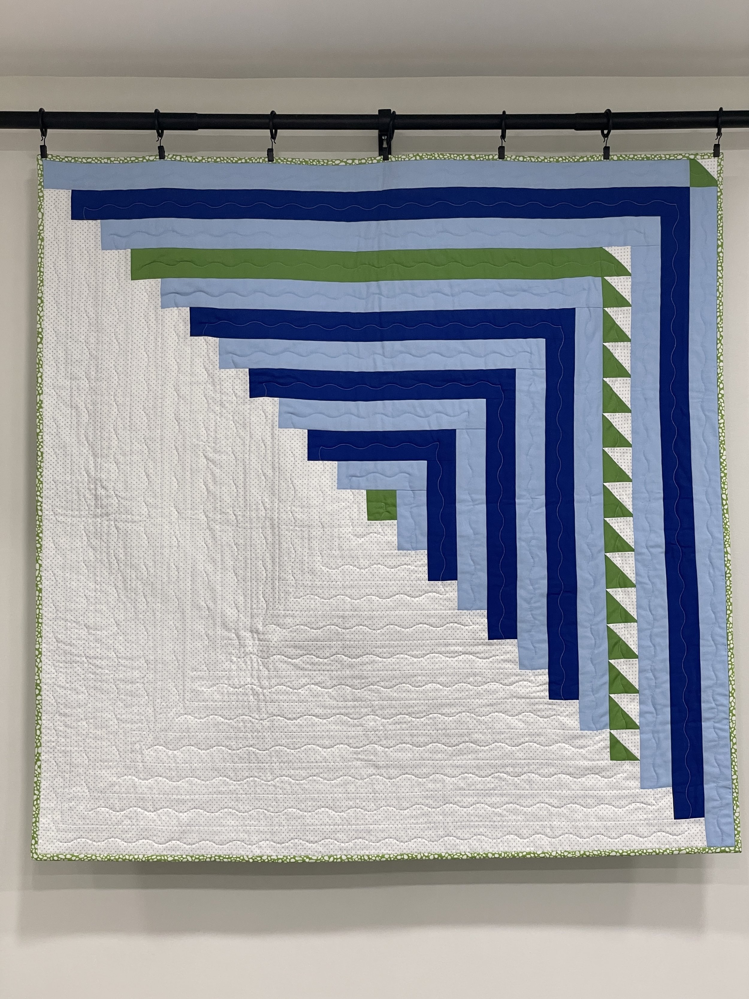 Striped quilt with blue, green, and white geometric patterns hanging on a rod.