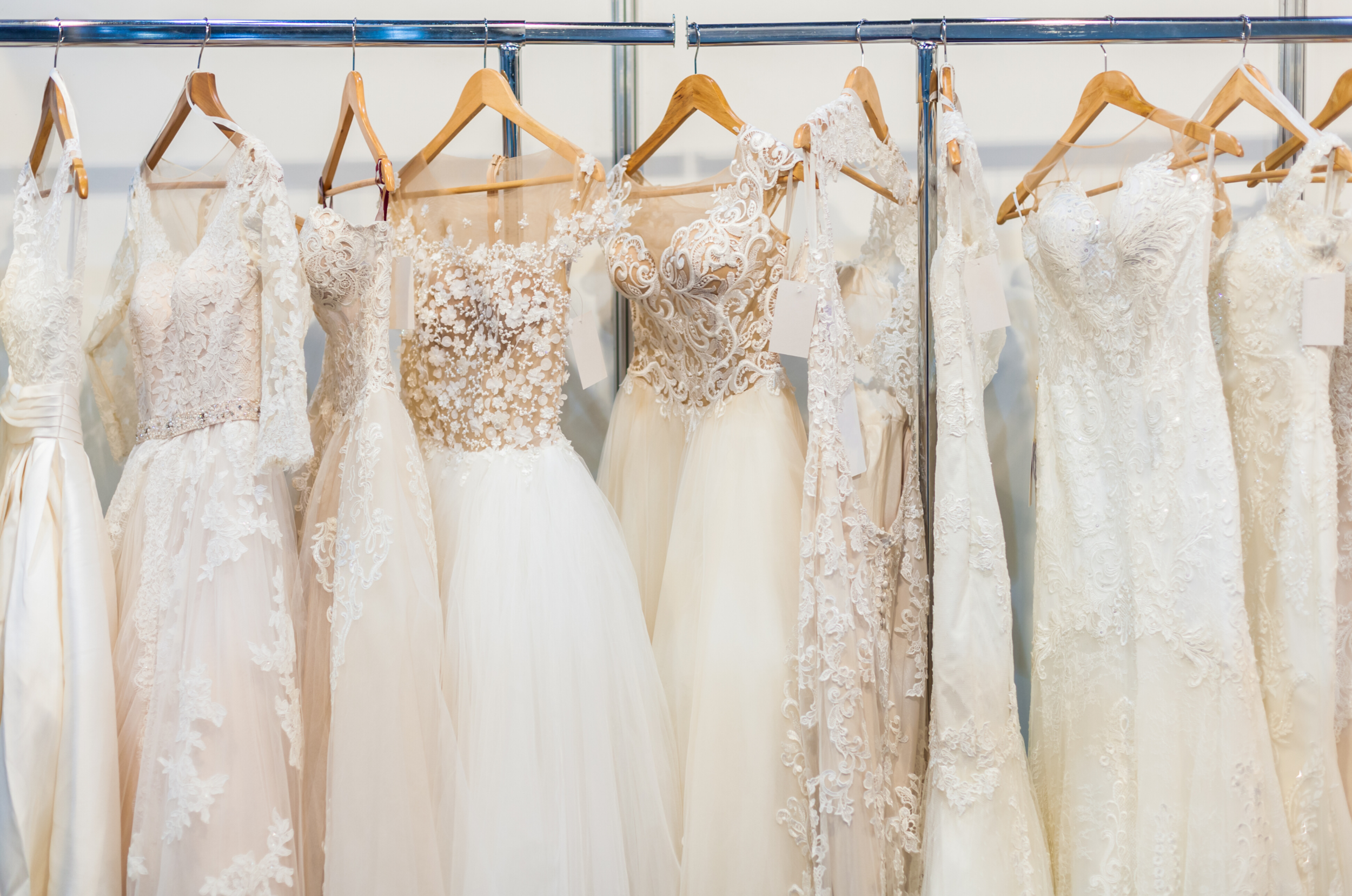 A row of white wedding dresses hanging on wooden hangers from a metal rack.