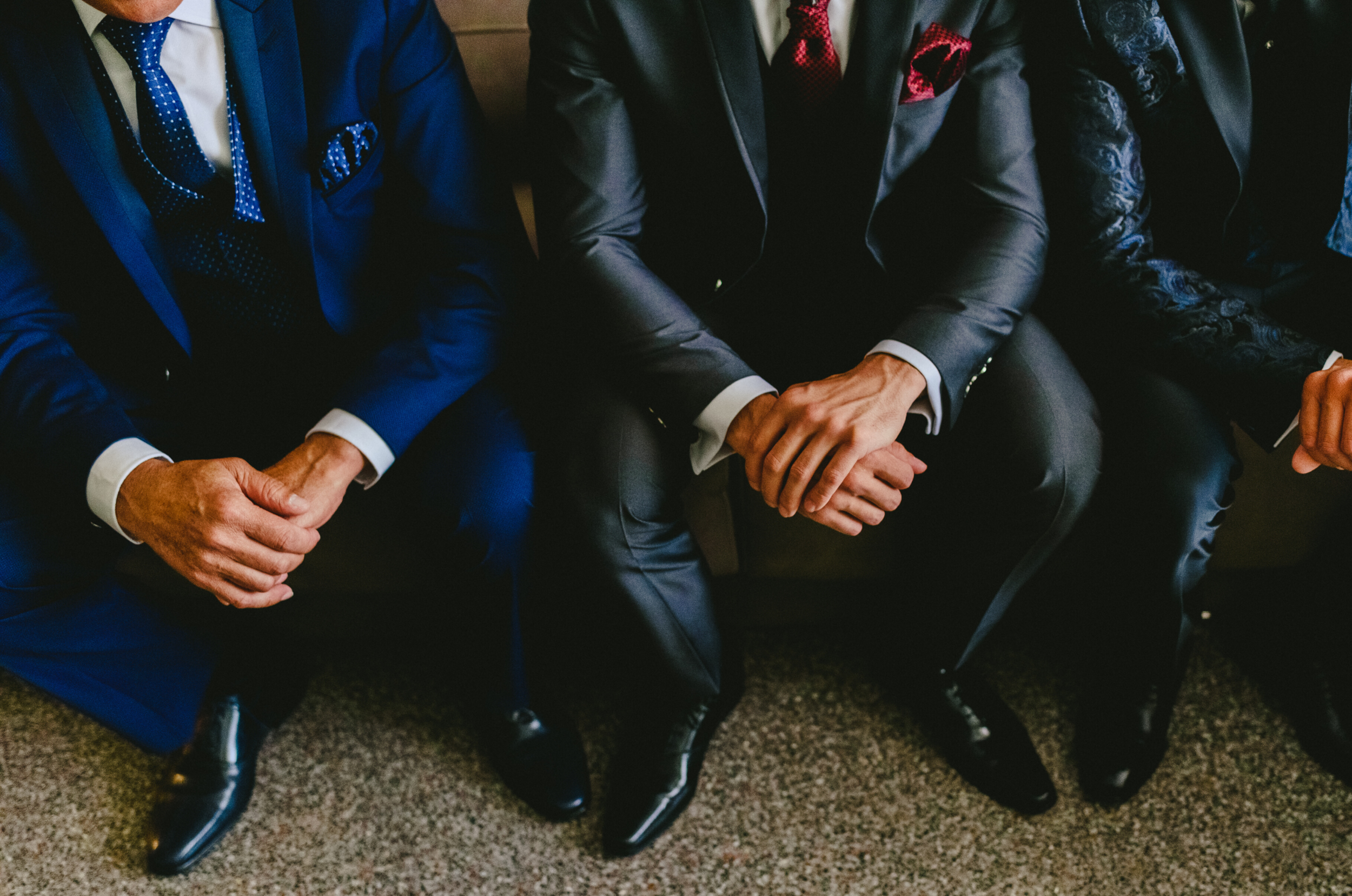 Three men in suits sitting with their hands clasped on their laps, dressed in formal attire.