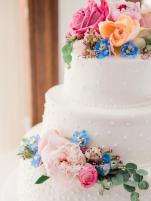 A white wedding cake decorated with pink, peach, blue, and purple flowers.