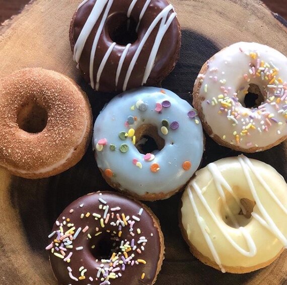 Six assorted decorated donuts on a wooden platter, with varieties of chocolate, vanilla, and colorful sprinkles.