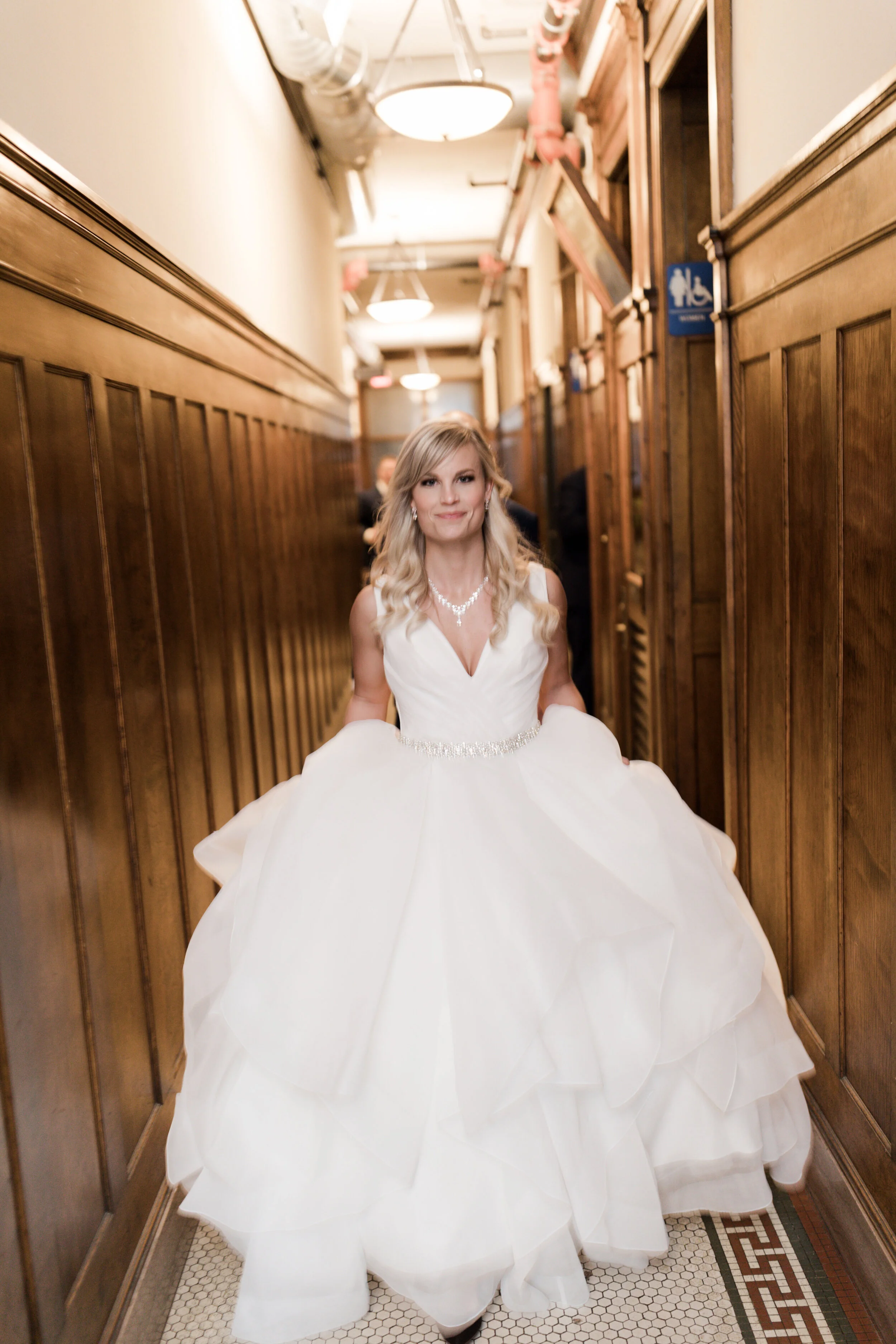 A woman in a wedding dress standing in a narrow hallway with wood-paneled walls.