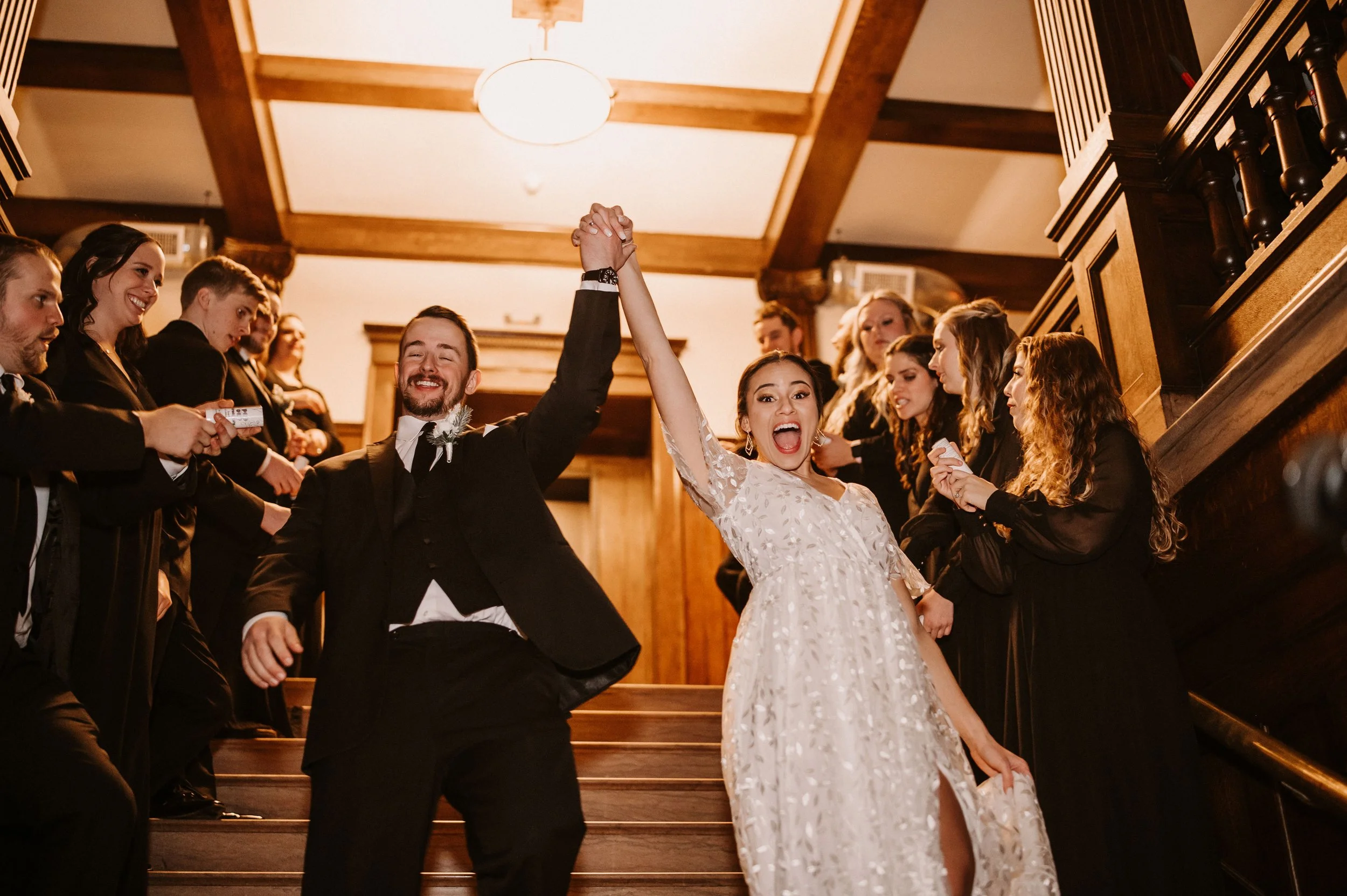 Bride and groom celebrating on a staircase surrounded by friends at a wedding reception.