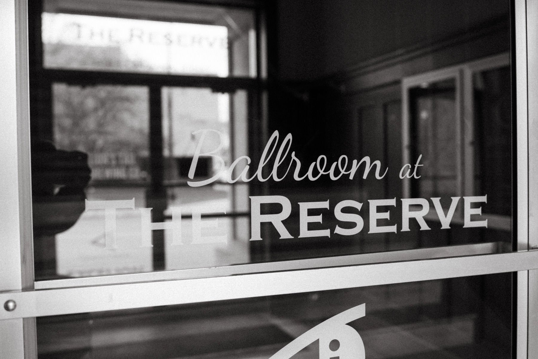 Glass door with the words 'Ballroom at The Reserve' written on it. The reflection in the glass shows the interior and an outside view.