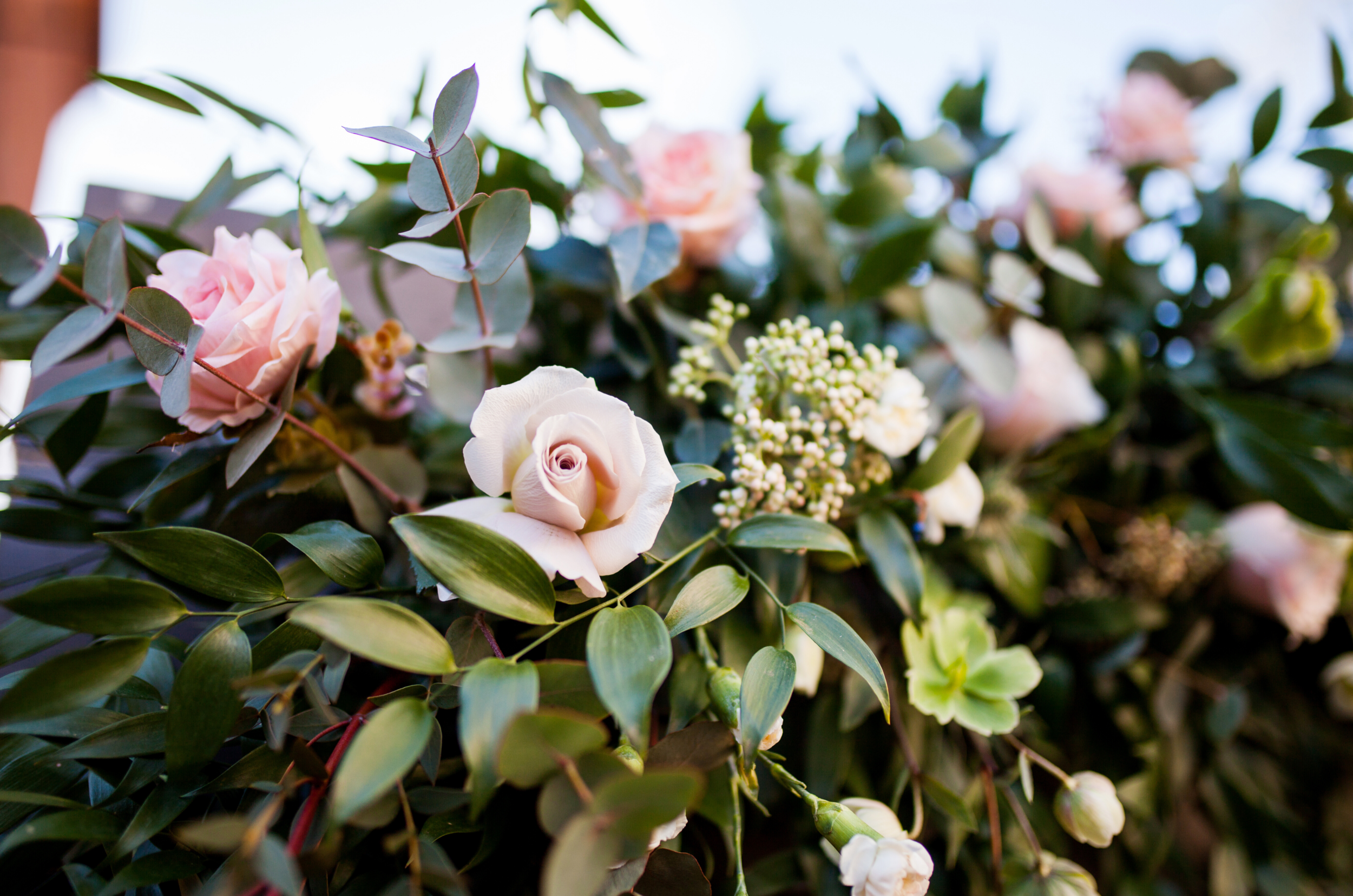 Close-up of a floral arrangement with pink and white roses, green leaves, and small white filler flowers.