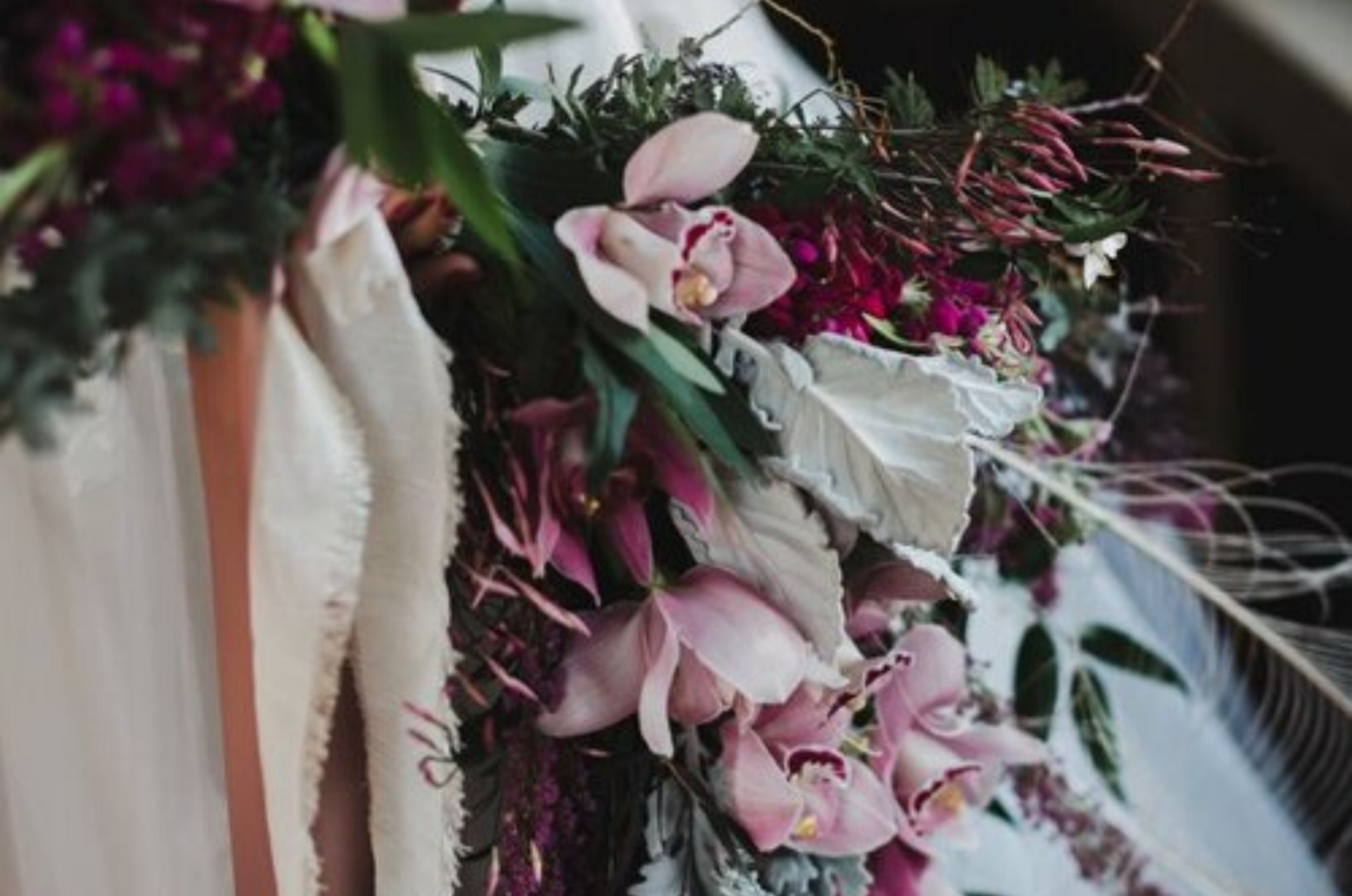 A close-up view of a floral arrangement with pink and white flowers, green leaves, and textured elements, placed on a wooden surface.