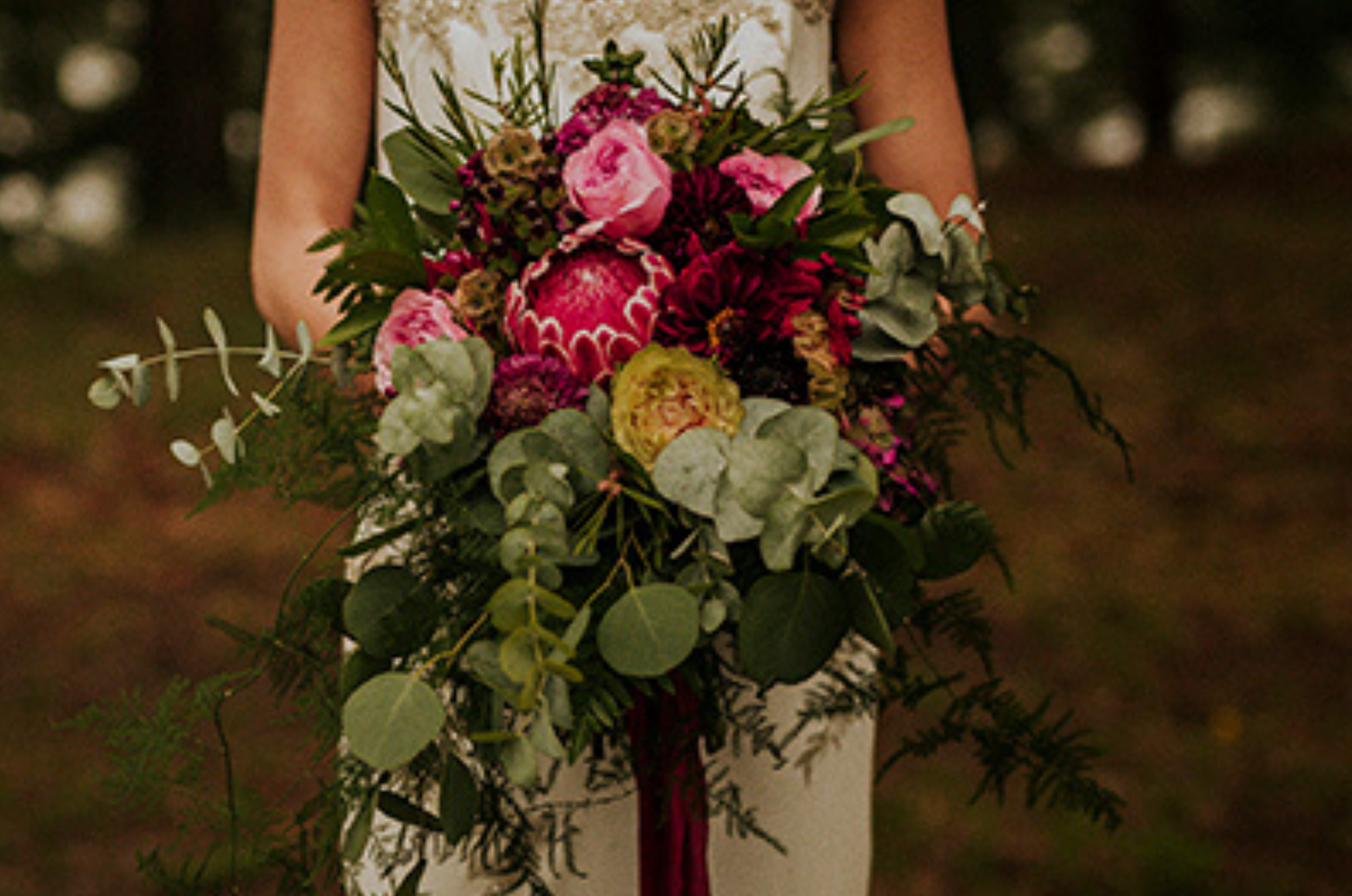 A woman holding a large, colorful bouquet of flowers outdoors.