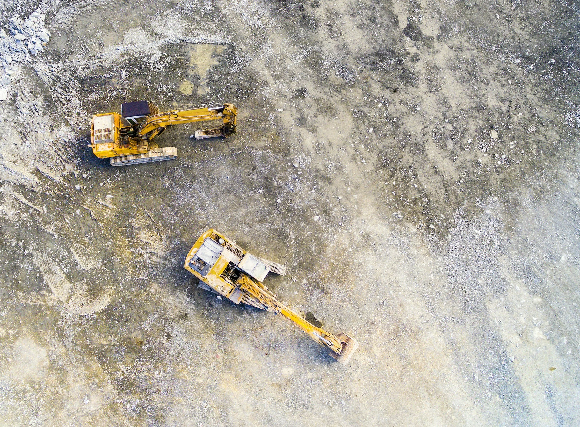 Aerial view of two yellow construction excavators working on a dirt surface at a construction site.