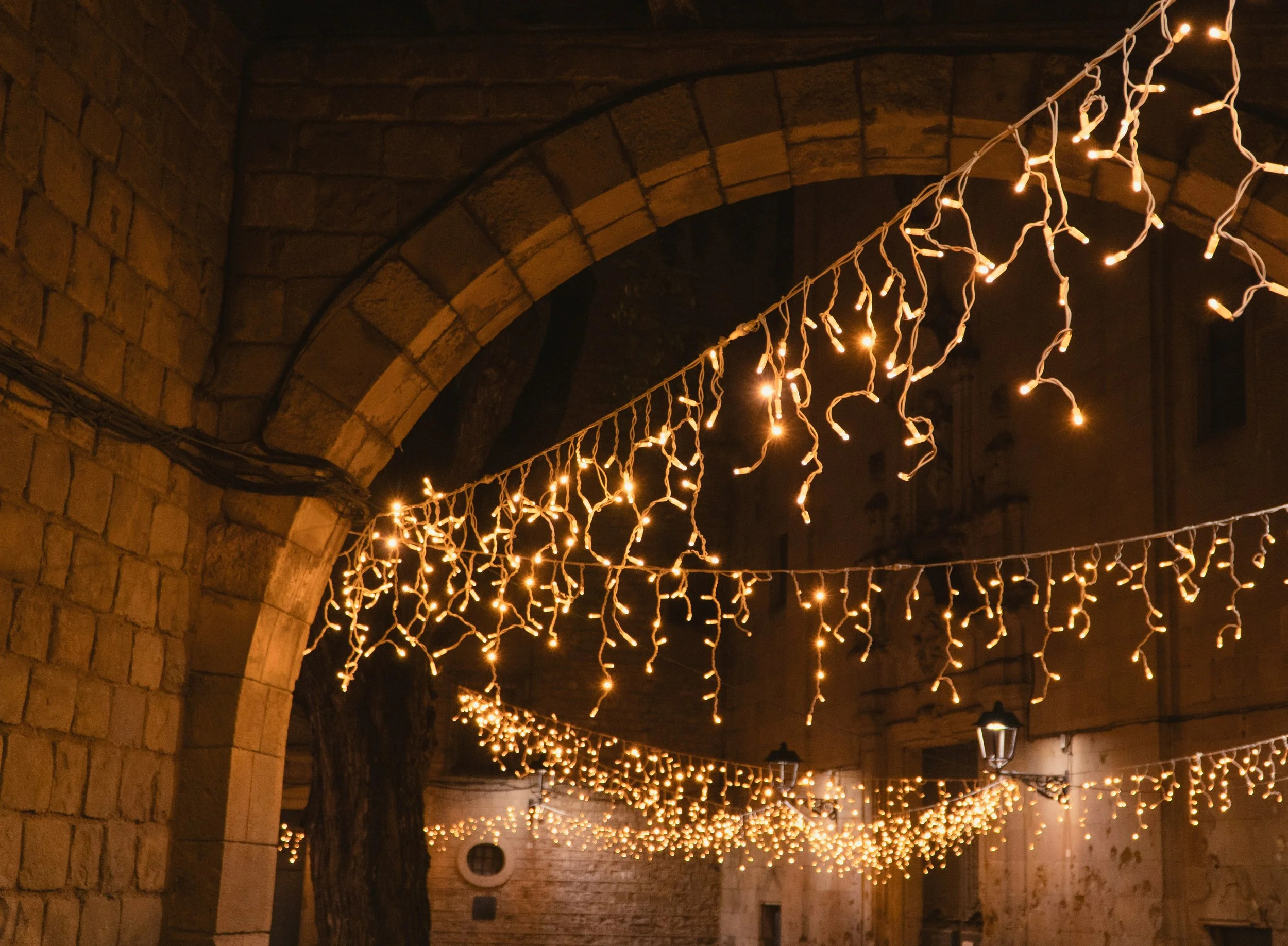 String of hanging string lights illuminating a stone archway at night.