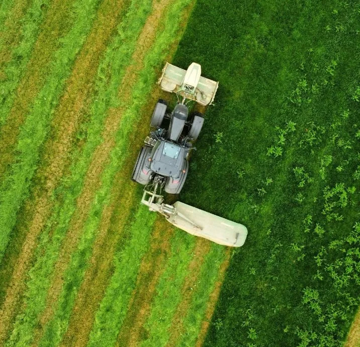 Aerial view of a tractor with a front loader and a harvester attached, working on a green farm field.