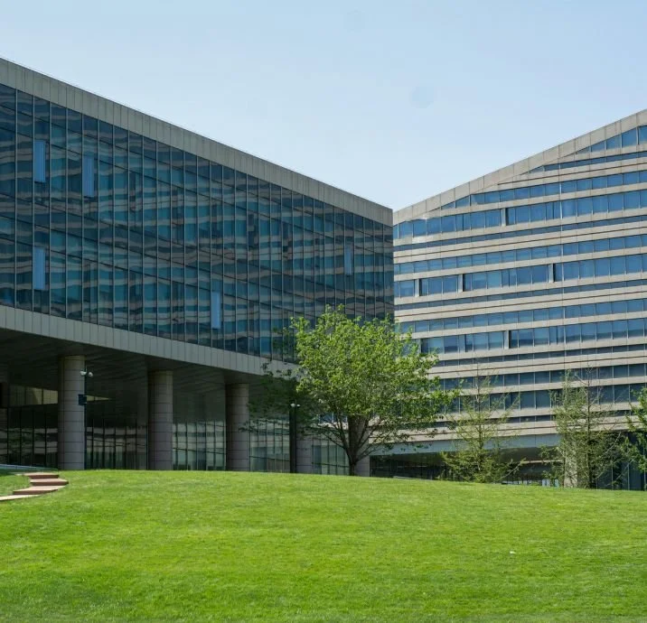 Modern office building with glass facade, surrounded by green grass and trees under a clear blue sky.