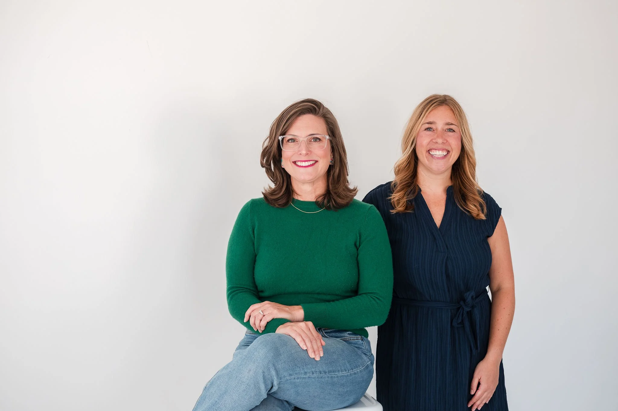 Two women smiling and standing against a plain white background.