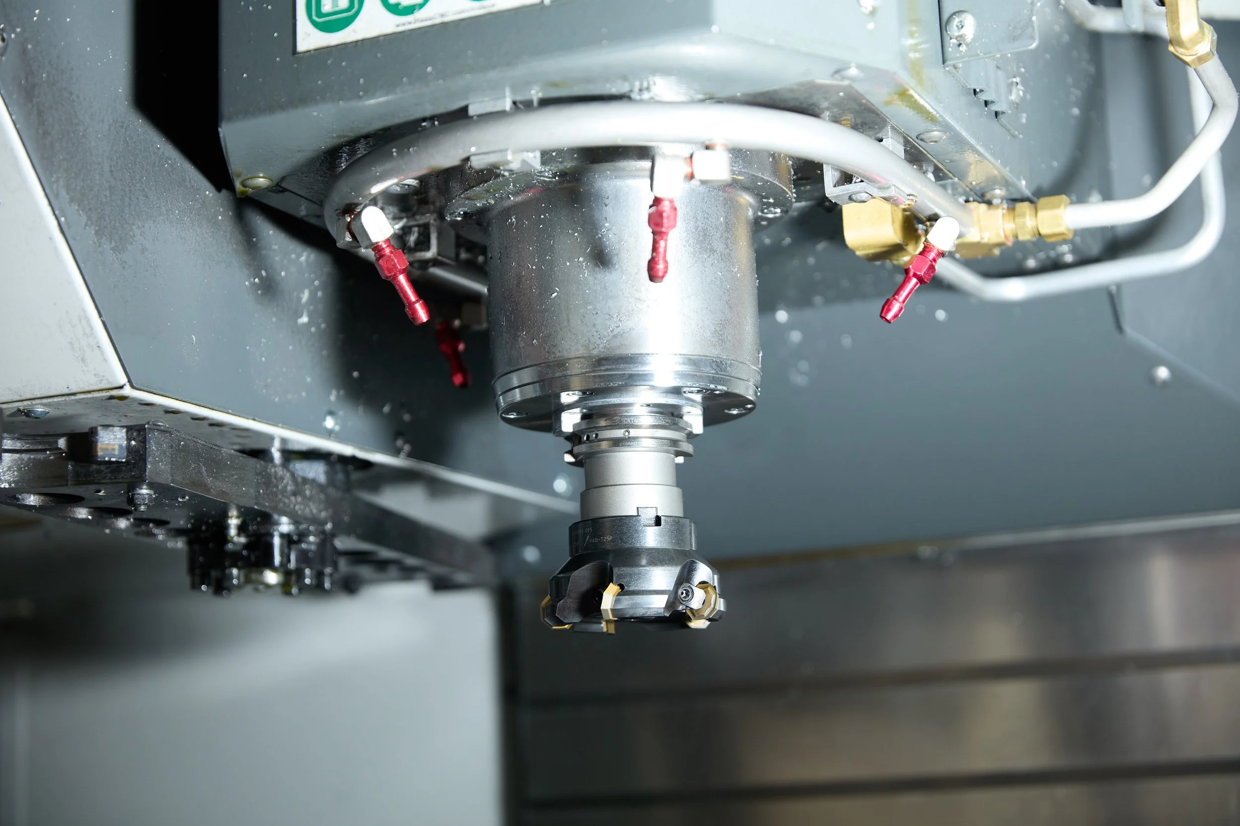Close-up of a CNC machine tool holder attached to the spindle of a machining center, with various coolant or hydraulic lines connected nearby.
