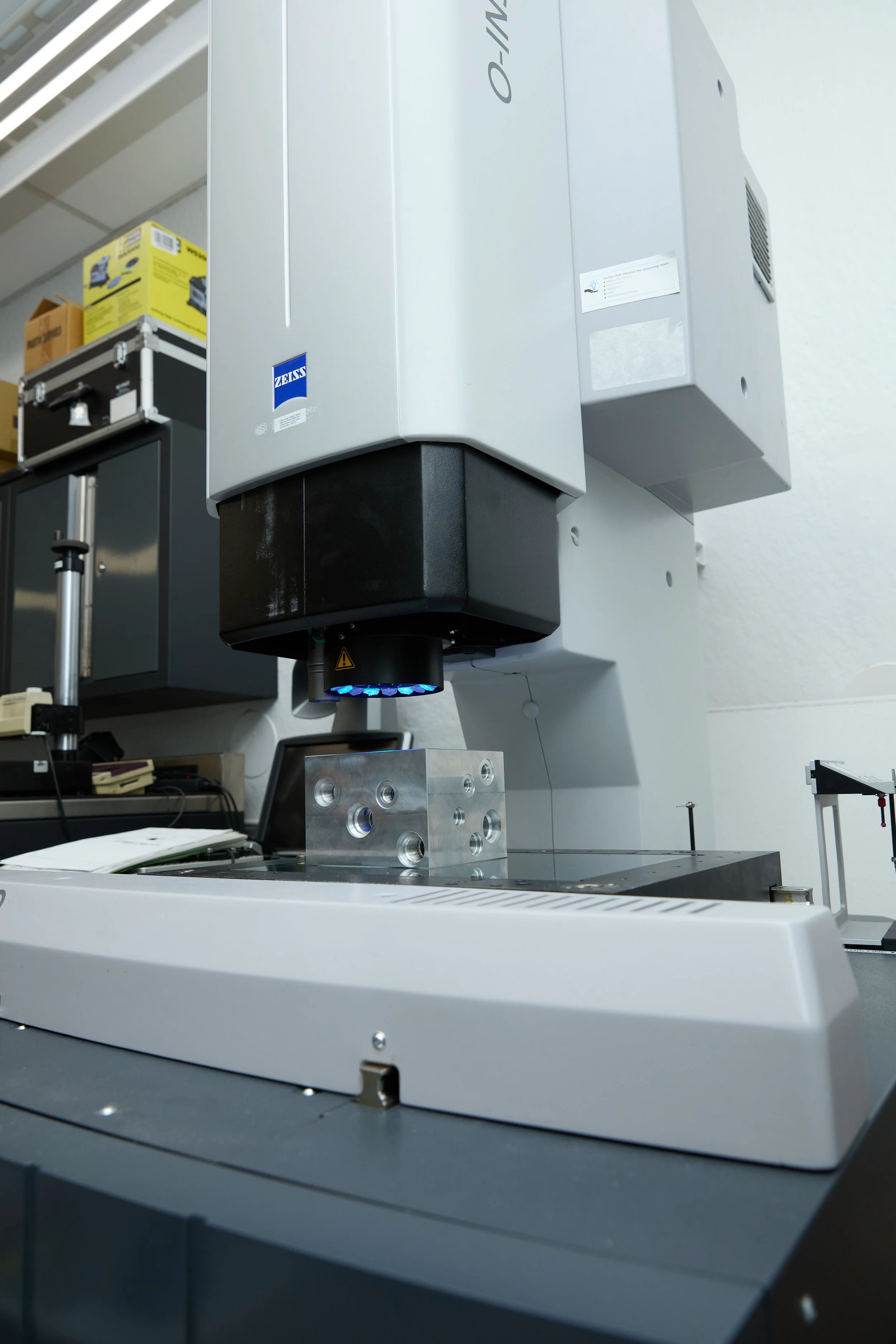 Scientific laboratory equipment, a microscope with a metallic sample holder on the stage, and other lab instruments and tools in the background.