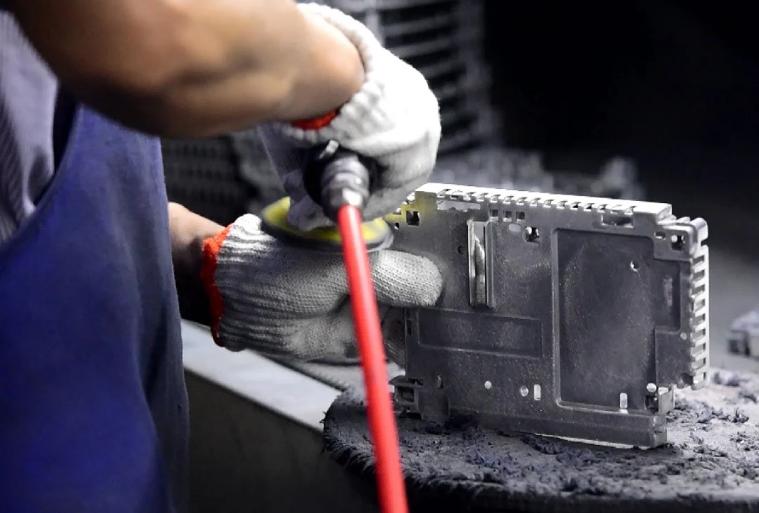 A worker in gloves polishing or grinding a metal or electronic component with a handheld power tool.