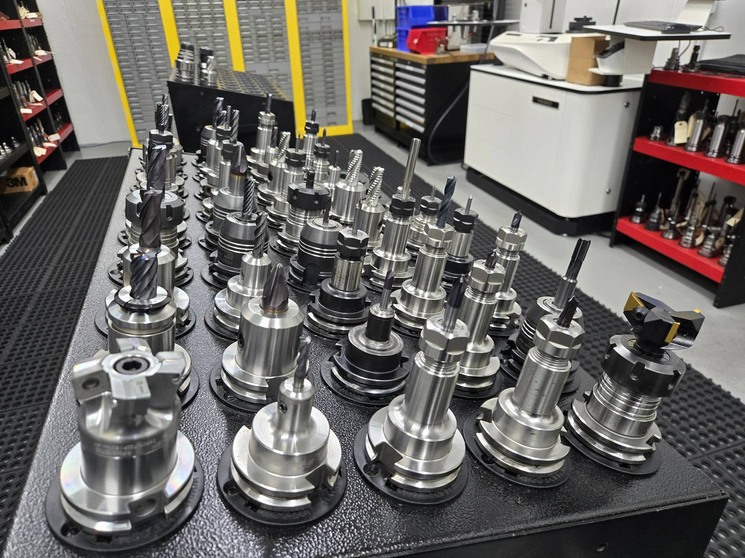 A collection of CNC machine tool holders and cutting tools organized on a workbench in a machine shop.