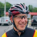 Smiling man wearing cycling helmet and glasses in a parking lot