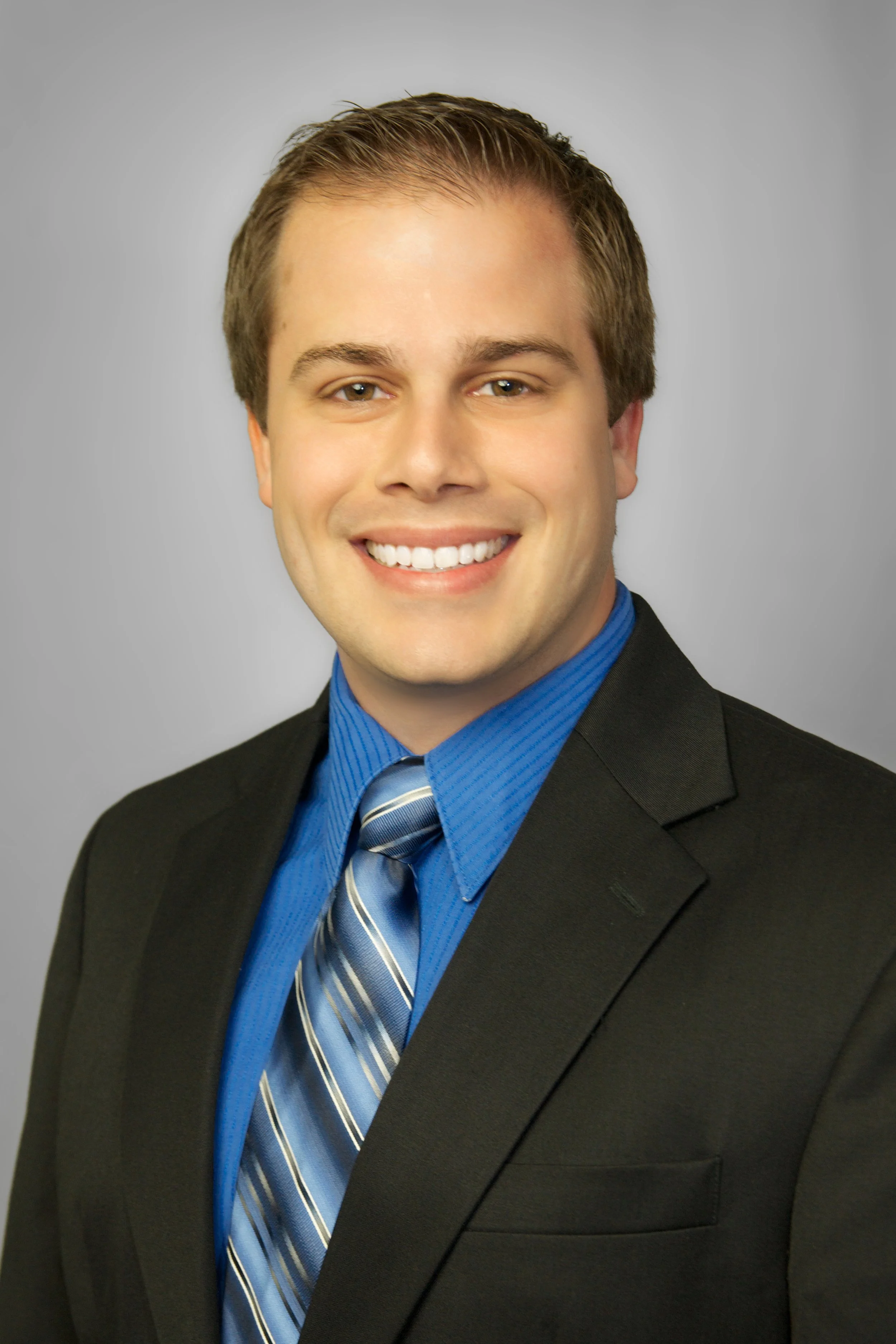 Professional headshot of Josh Morris wearing a black suit, blue shirt, and striped tie, smiling against a gray background. As a CPA with a focus on tax planning and tax strategies, he looks to reduce taxes for professionals and business owners.