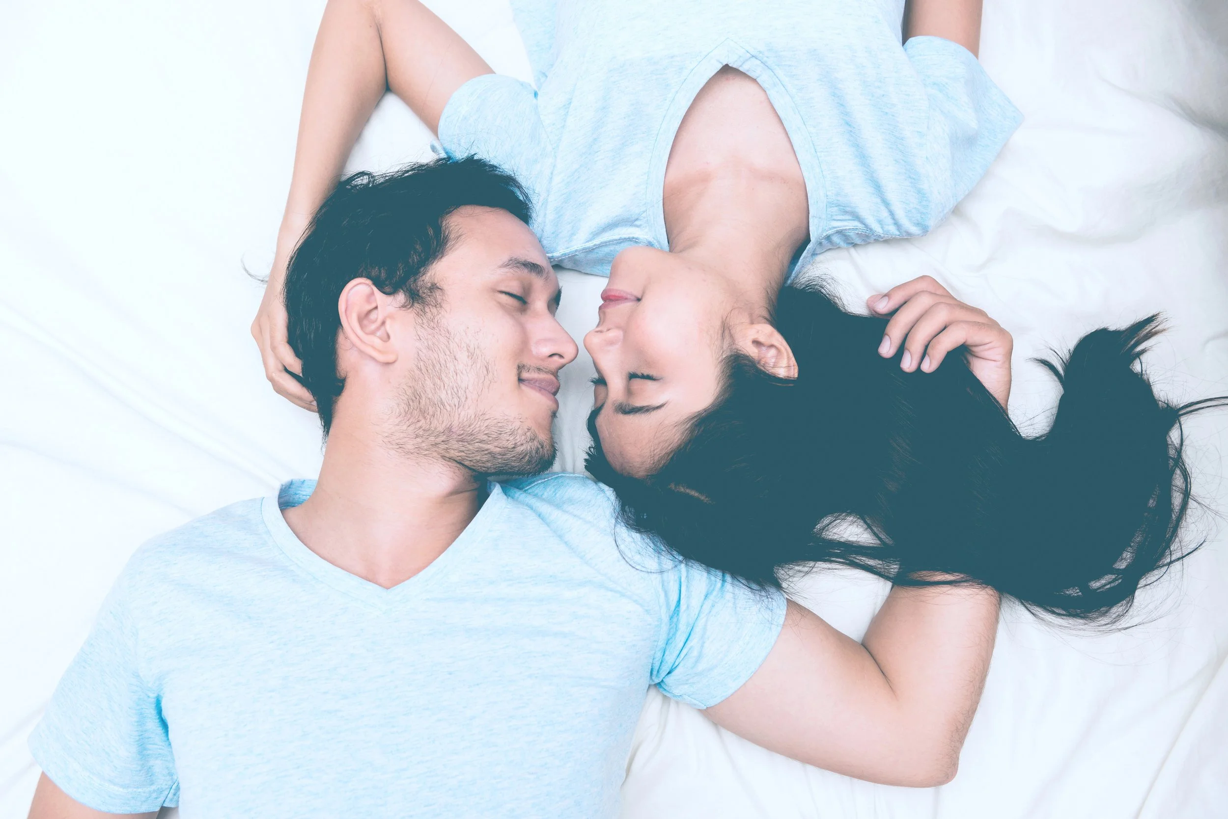 Top view of smiling man and woman lying with their faces together and their bodies spread away.