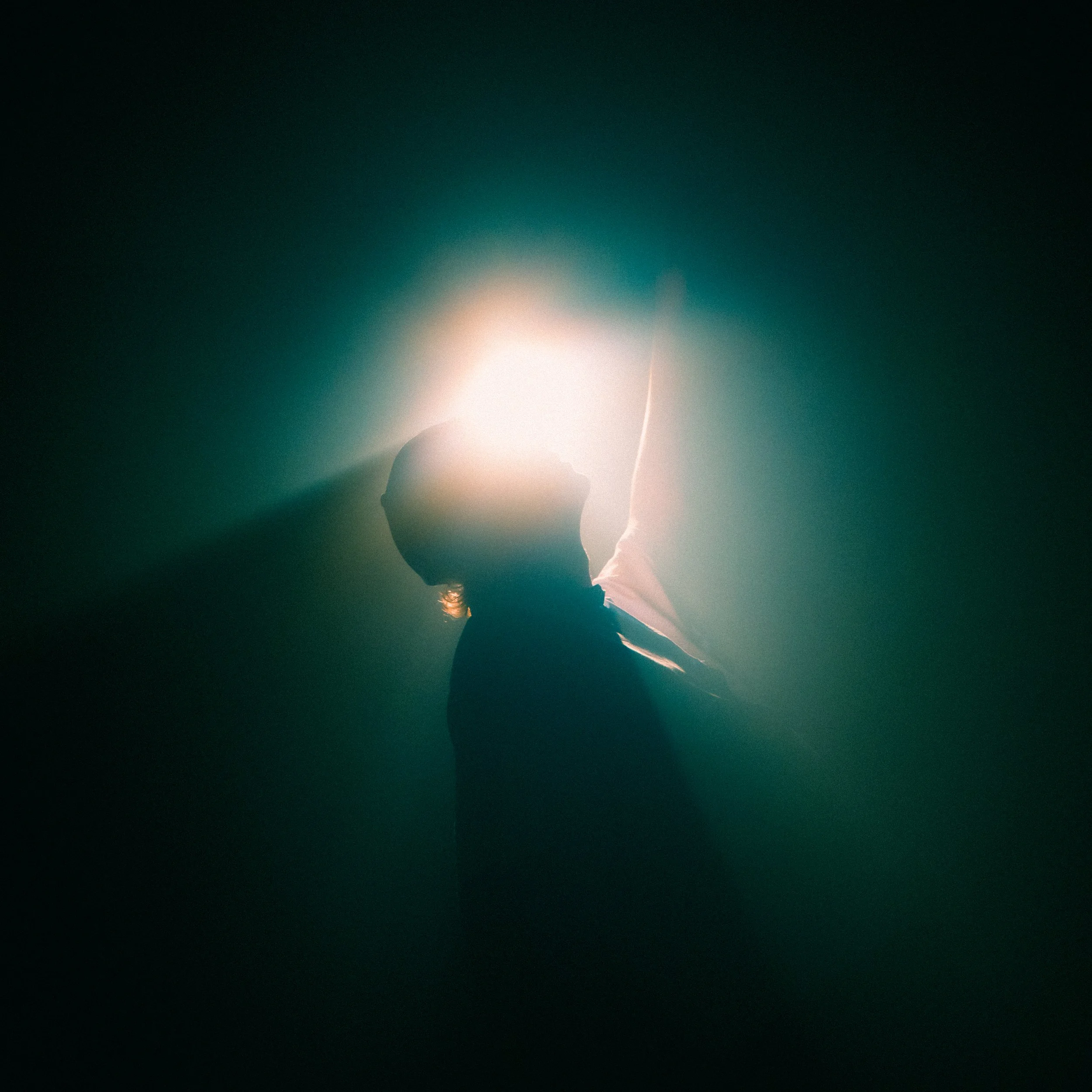 Silhouette of a person with one arm raised, backlit by a bright light creating a glowing halo effect.