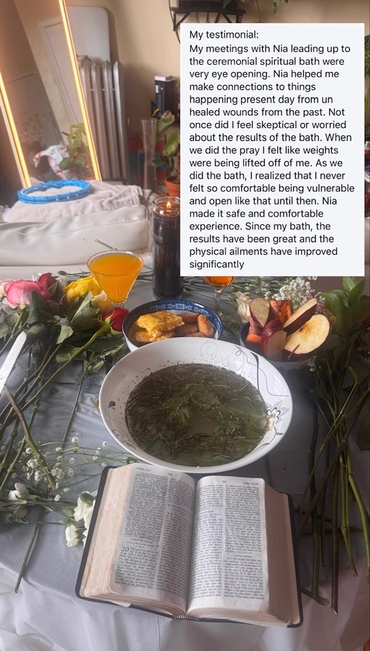 Table set with flowers, a large bowl of herbal tea, a Bible, a glass of orange juice, a glass of wine, a small plate with bread and food, and a candle. There is a mirror and some books in the background.