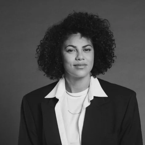 Black and white portrait of a woman with curly hair wearing a blazer and white shirt.