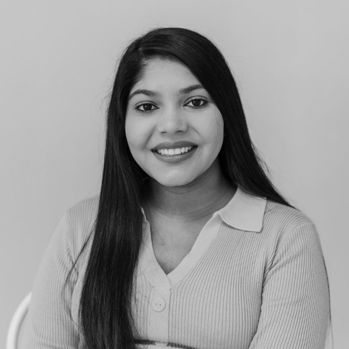 Black and white portrait of a young woman with long, straight hair smiling at the camera, wearing a light-colored, collared, ribbed sweater, against a plain background.