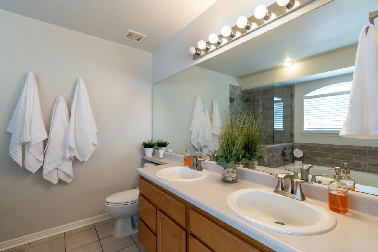 Bathroom with double sink vanity, large mirror, white towels on wall, potted plants, and a shower and bathtub in the background.