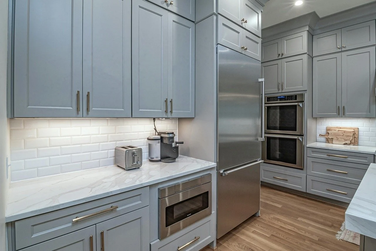 Modern kitchen with blue cabinets, white marble countertops, stainless steel appliances, and white subway tile backsplash, with wooden flooring.
