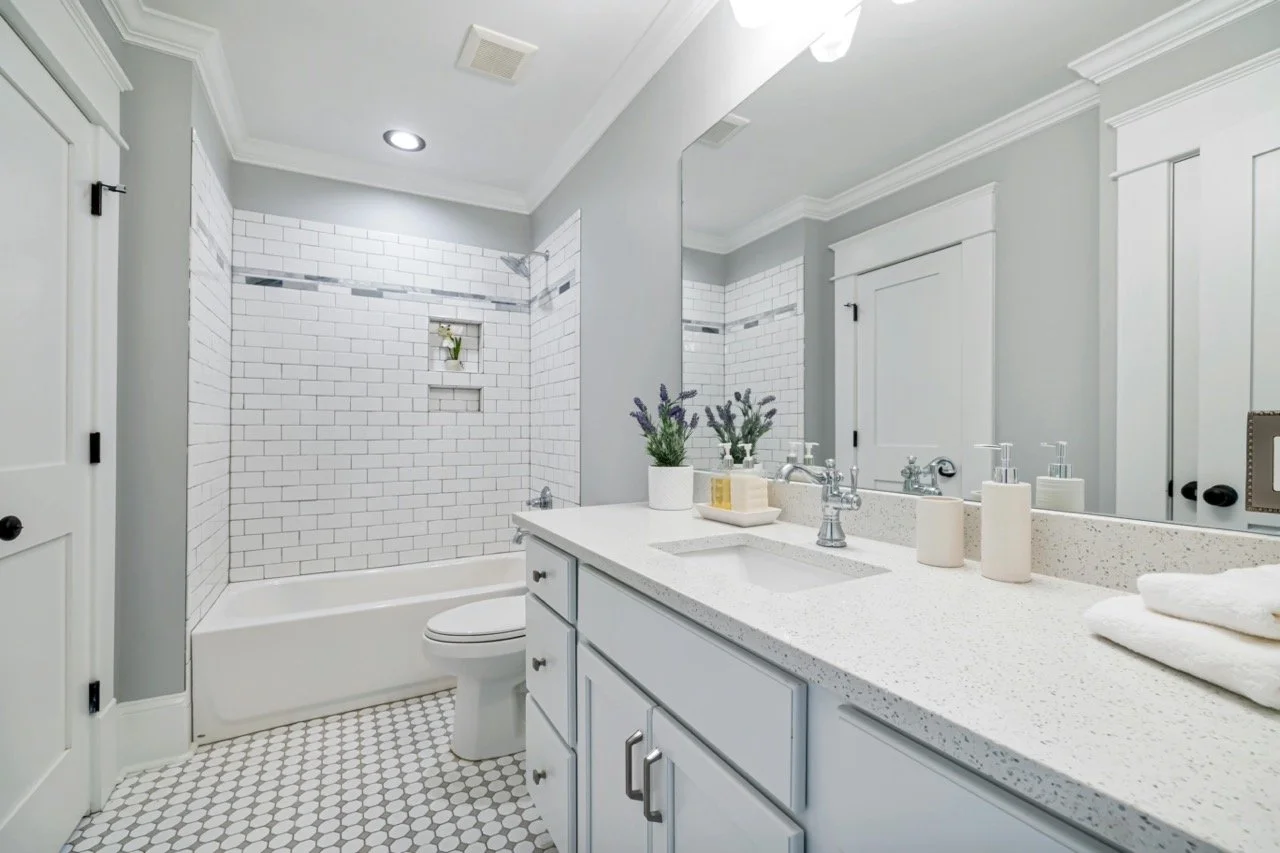 Modern bathroom with white subway-tiled shower, white vanity with speckled countertop, and decorative plants.